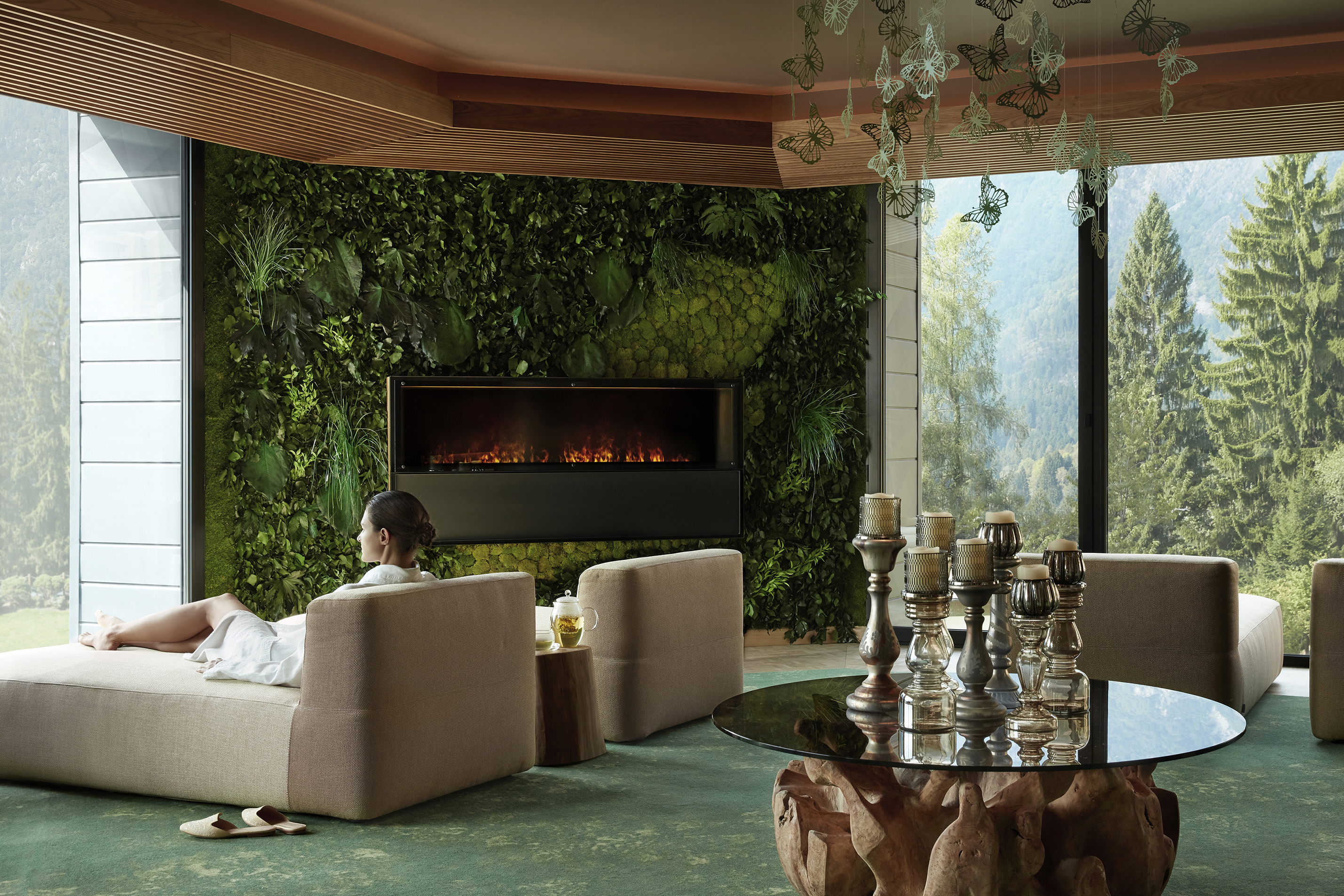 Woman sat on plush lounge chairs in the spa relaxation room decorated with a plant wall and multiple candles on a driftwood table