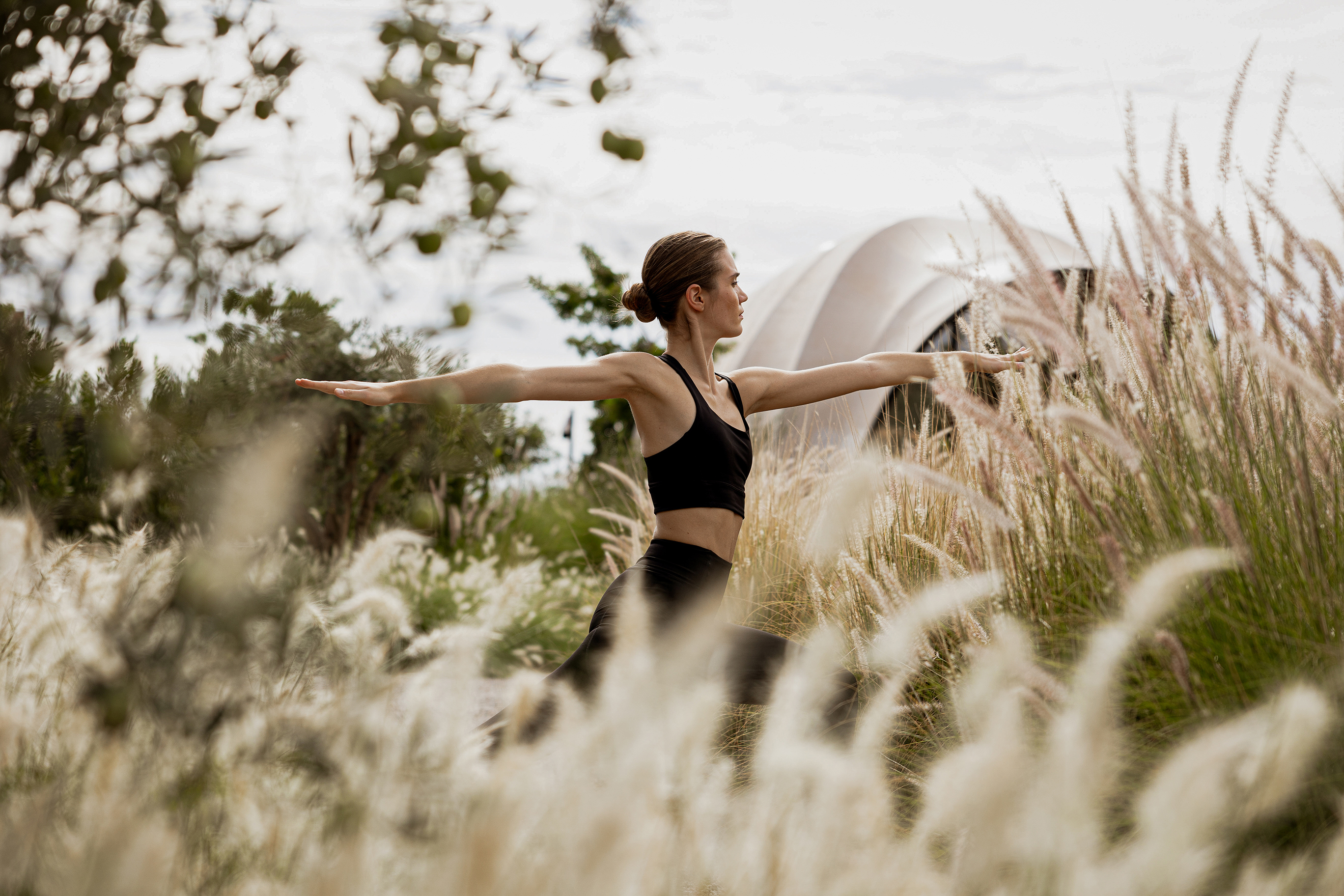A woman in black exercise clothing practicing yoga among pampas grass