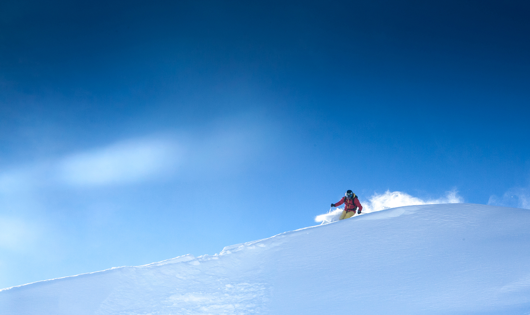 Skier leaving powder spray in snow against blue sky