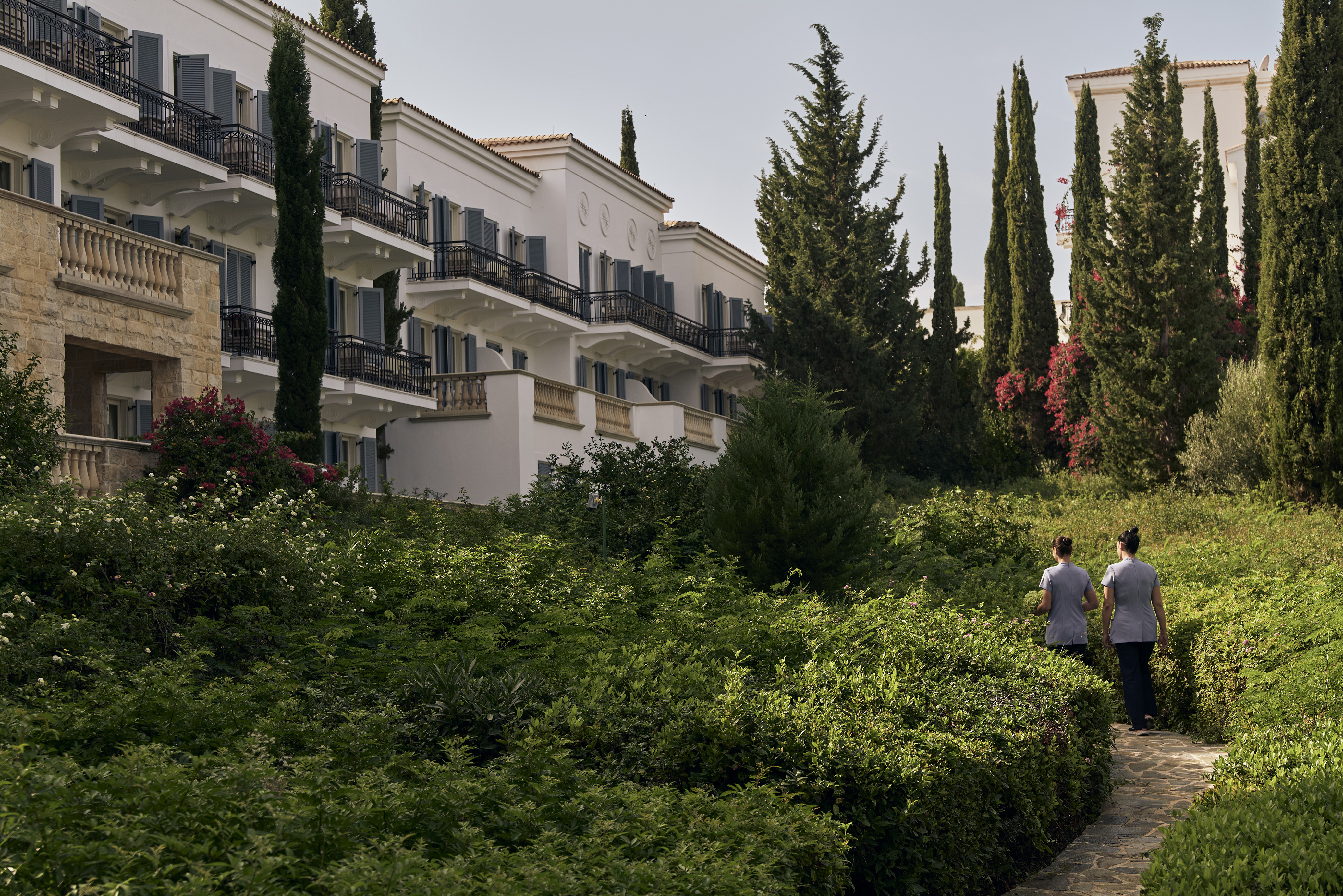 Two staff members walking a narrow pathway at Anassa in Cyprus with the hotel behind
