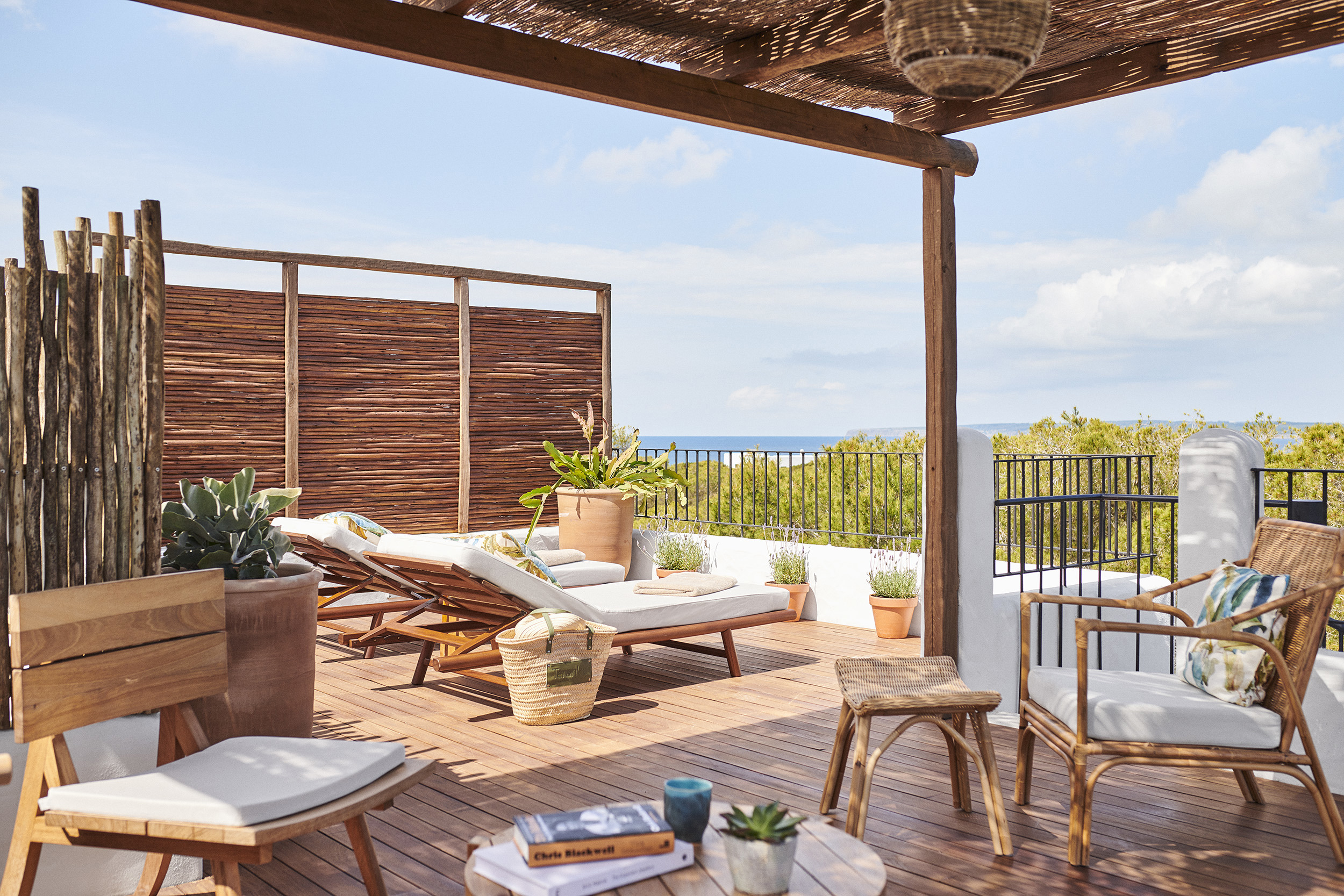 The rooftop of a one bedroom suite with open-air sun loungers surrounded by plant pots and a coffee table and rattan chairs beneath a woven canopy