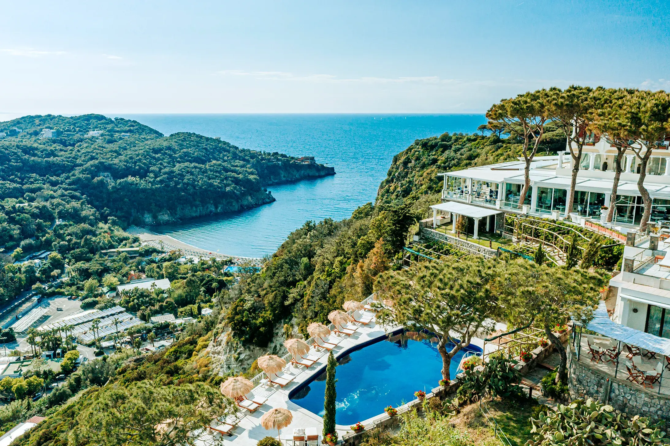Bird's eye view of the luxurious pool area at San Montano Resort on Ischia overlooking the Mediterranean Sea and lush green hills.