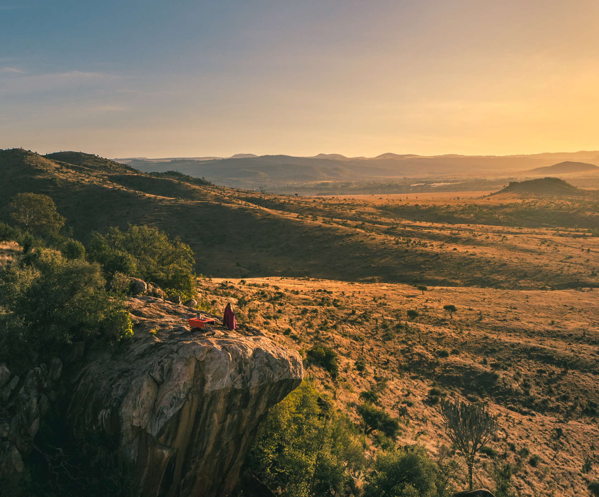 Person stood on a rock overlooking a rugged landscape of grass and shrubs