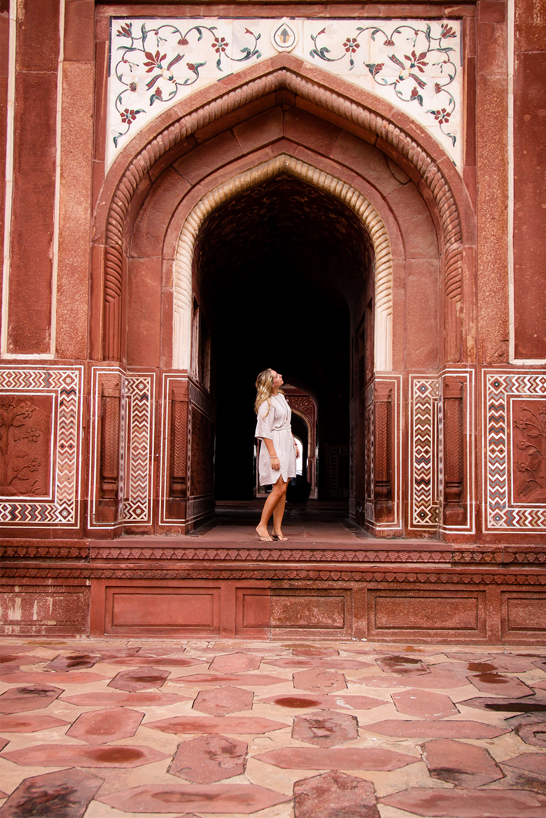 A young woman stands at the entrance of an ornate arched doorway with intricate designs, at what appears to be a historical building.
