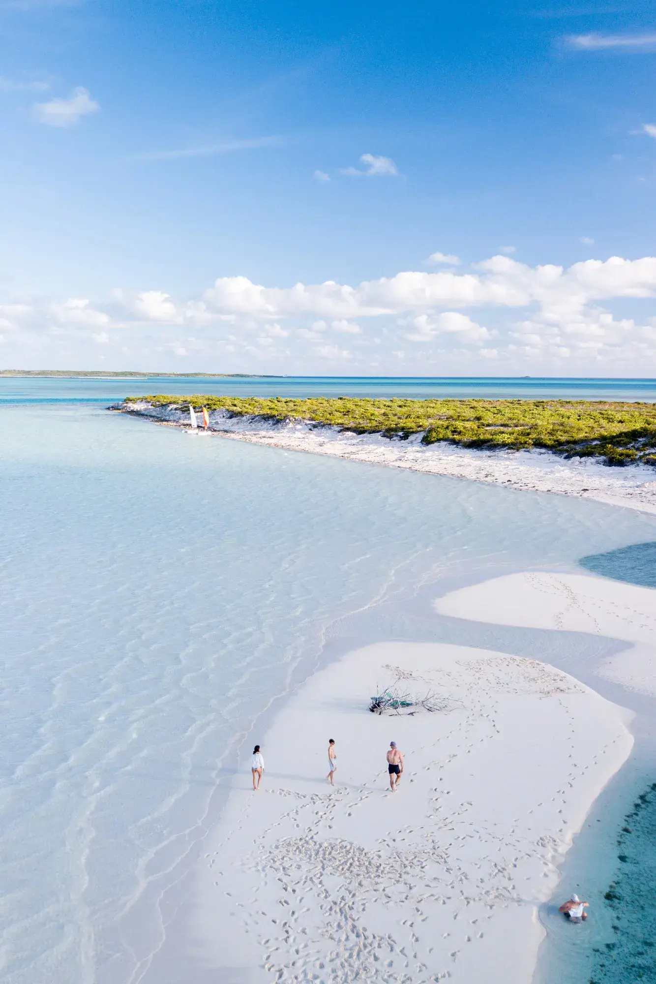 Three people enjoying a secluded beach on Little Ambergris Cay beneath a sunny sky