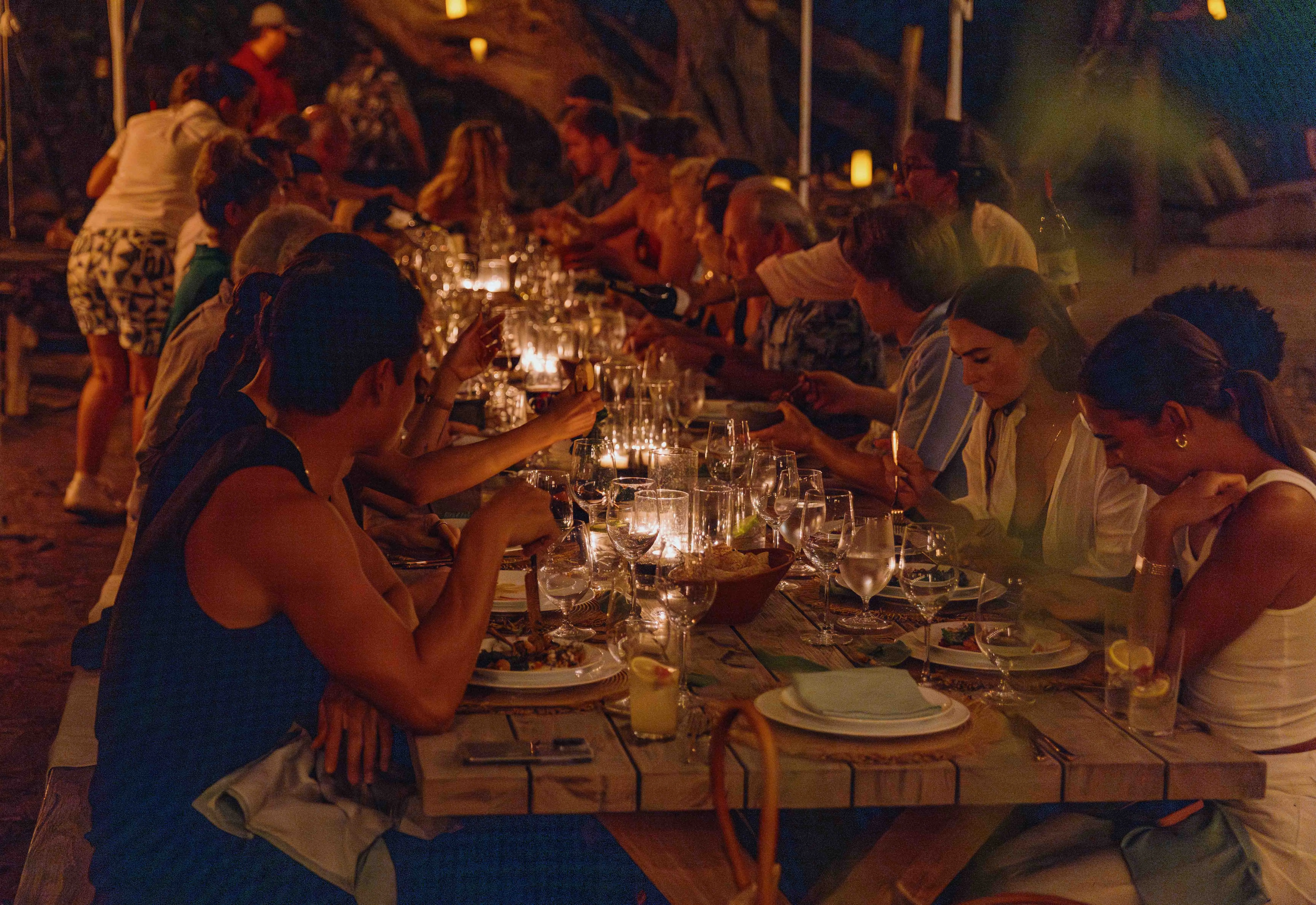 Several guests gathered around a communal dining table set for a feast at night