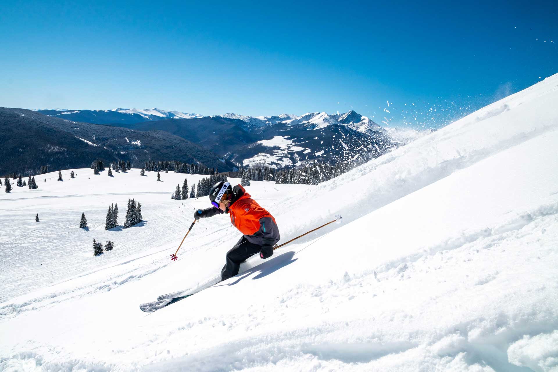 A person skiing downhill with mountains in the background