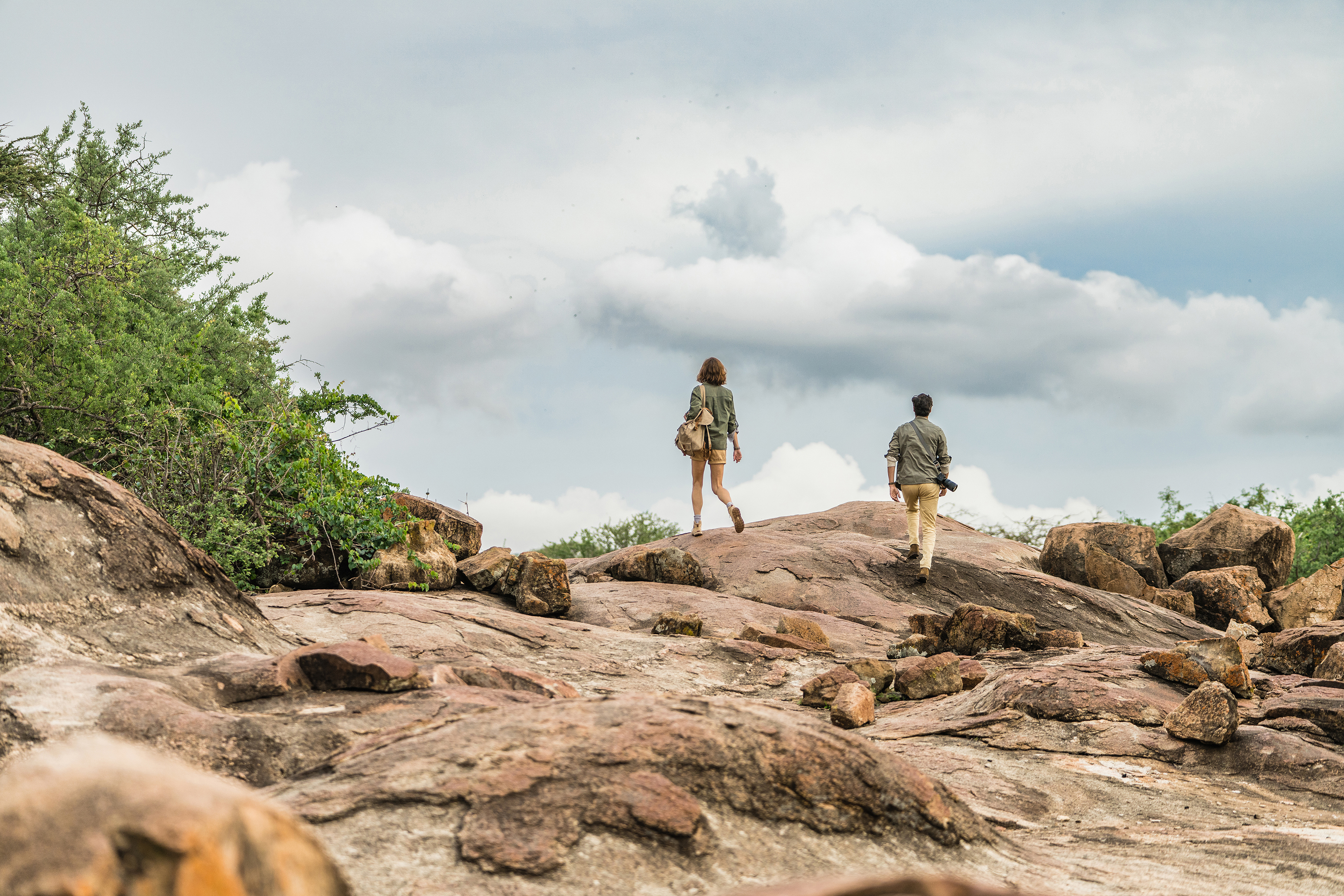 A man and a woman hiking to the top of a rock formation beneath a blue sky dappled with clouds
