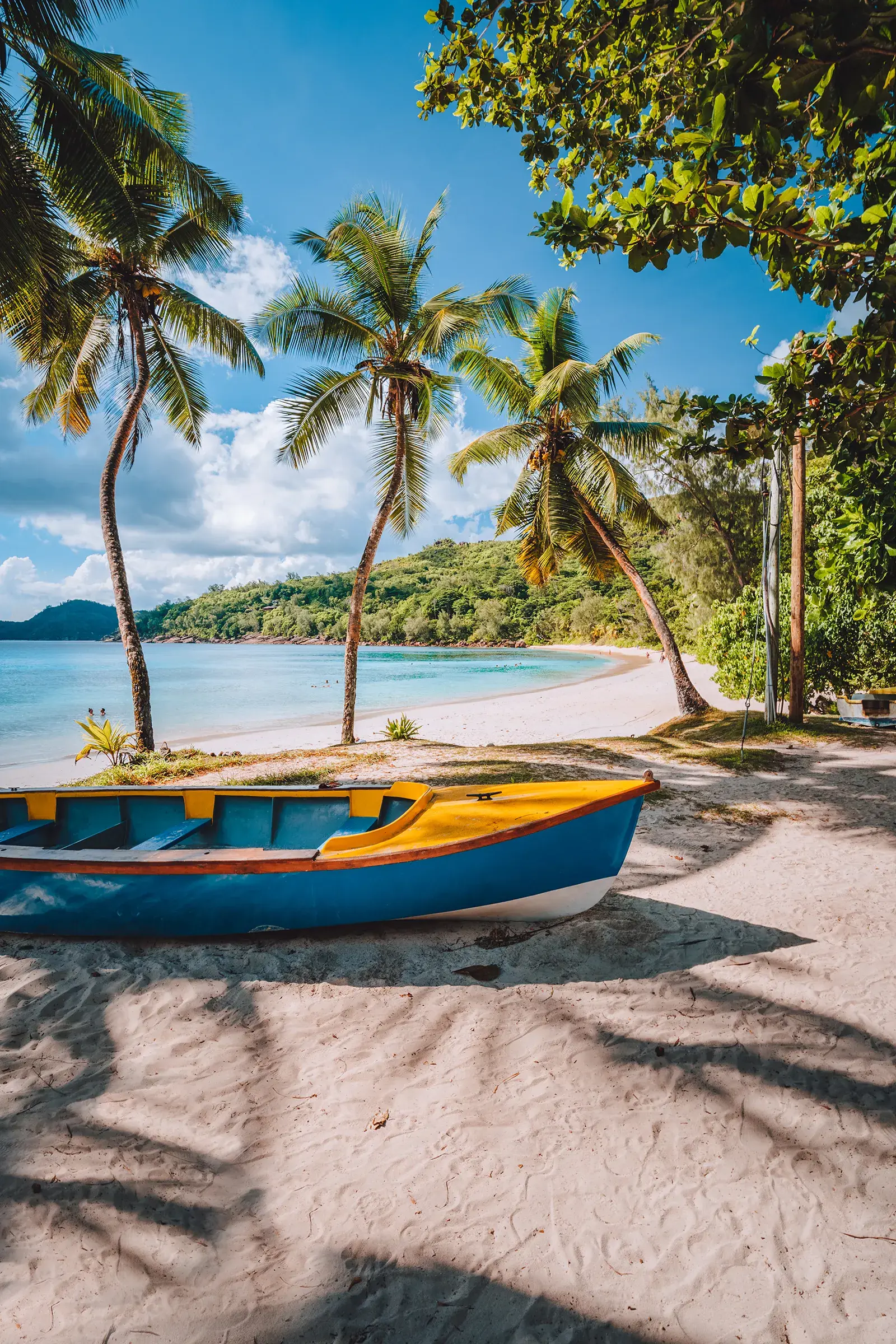 Tropical beach scene with palm trees, soft white sand and a colorful boat beside clear blue water.