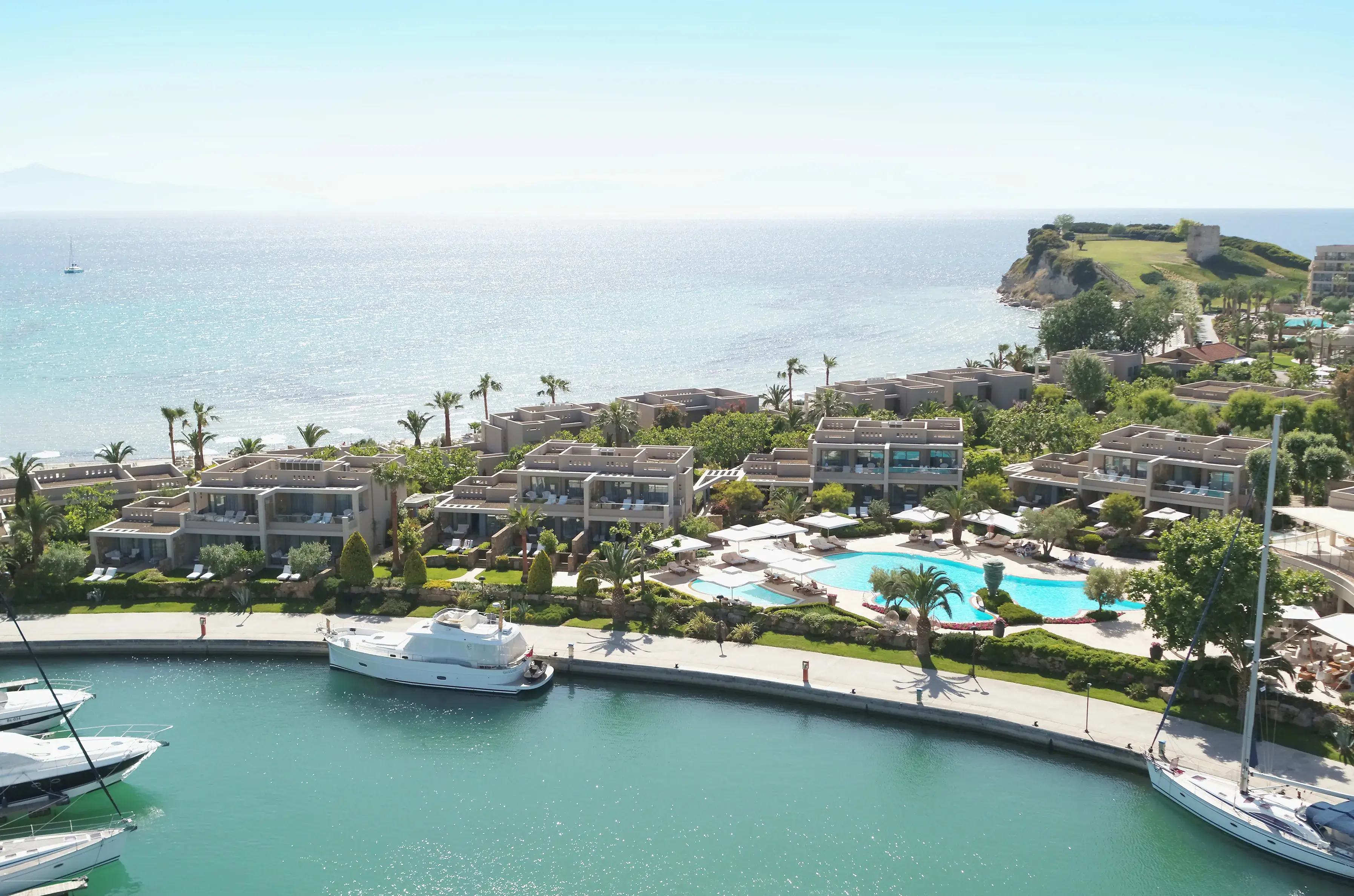 Aerial view of Sani Asterias in Halkidiki featuring luxury suites, a turquoise pool, lush gardens and a marina overlooking the Aegean Sea.