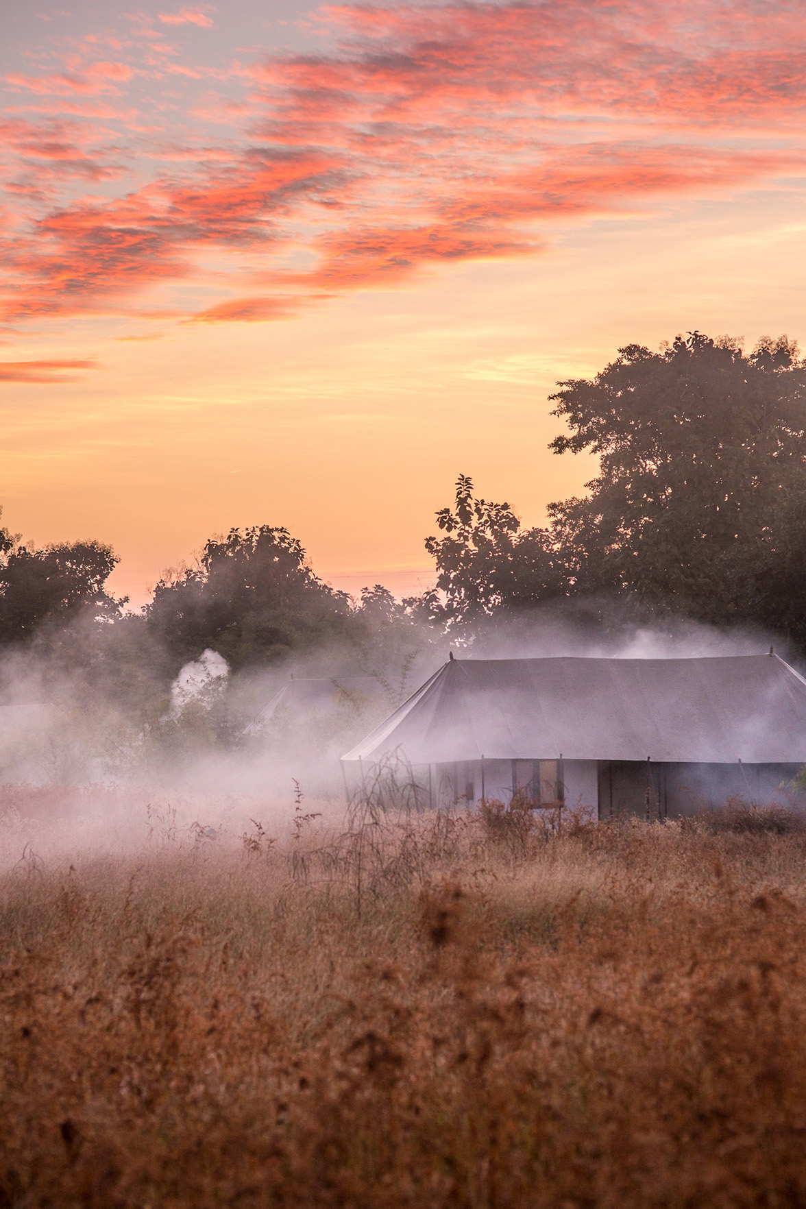 Asia, India, smoke over tented accommodation with sunset in background