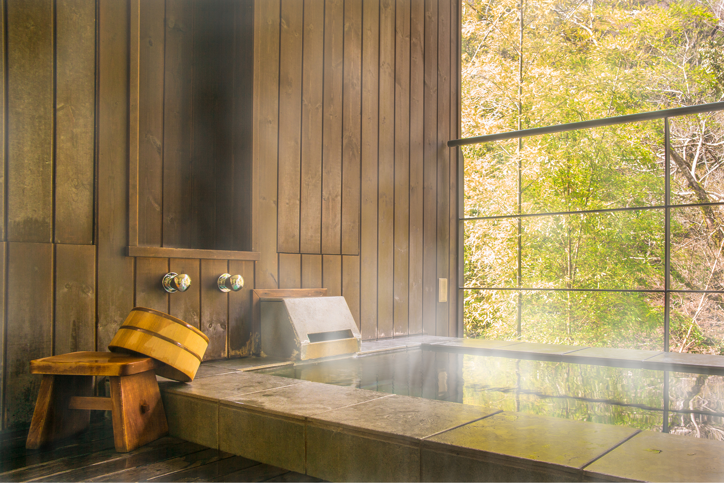 A traditional steaming Japanese onsen bath in a wood-panelled room overlooking green gardens