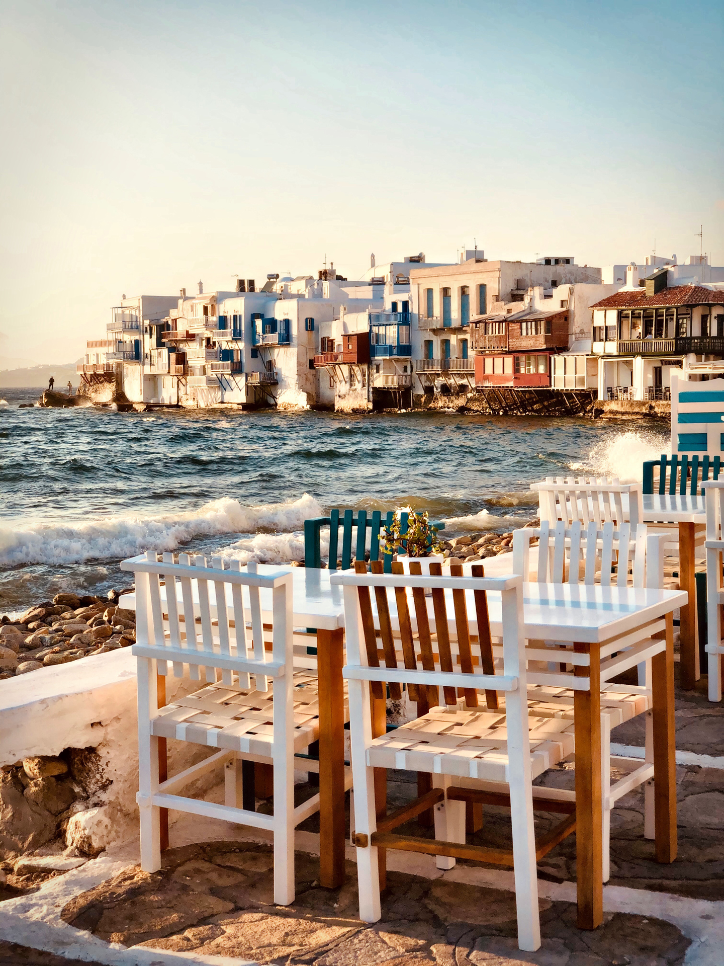 Chairs and tables next to the sea with buildings in the background