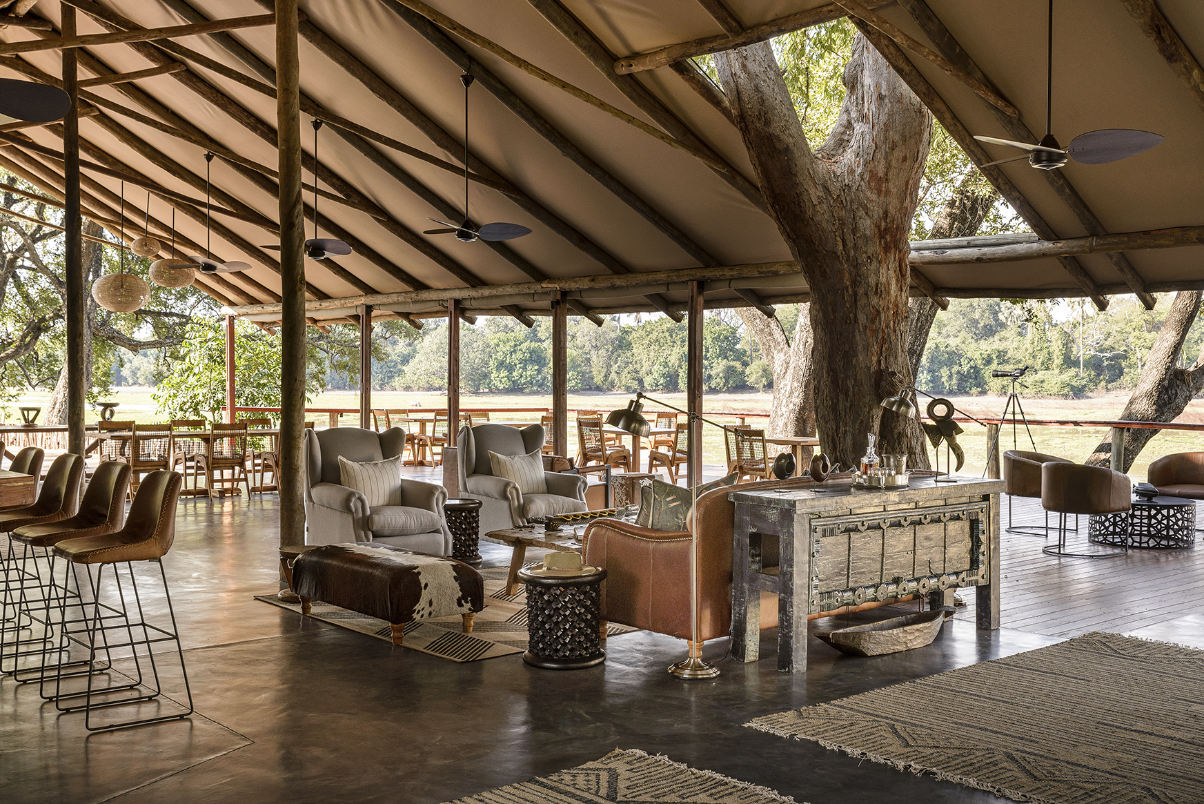 Africa, Zambia, Sungani Lodge, sofas, armchairs, table seating and bar stools on the main deck covered by a roof of wooden beams and canvas