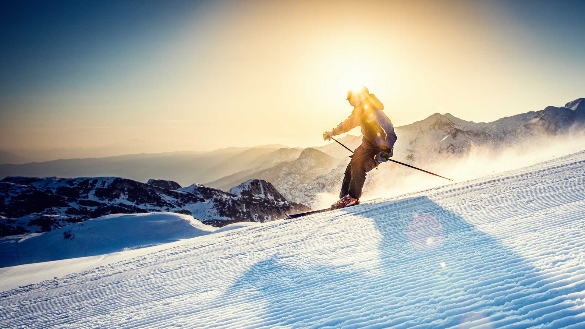 A skier going downhill as the sun shines from behind them