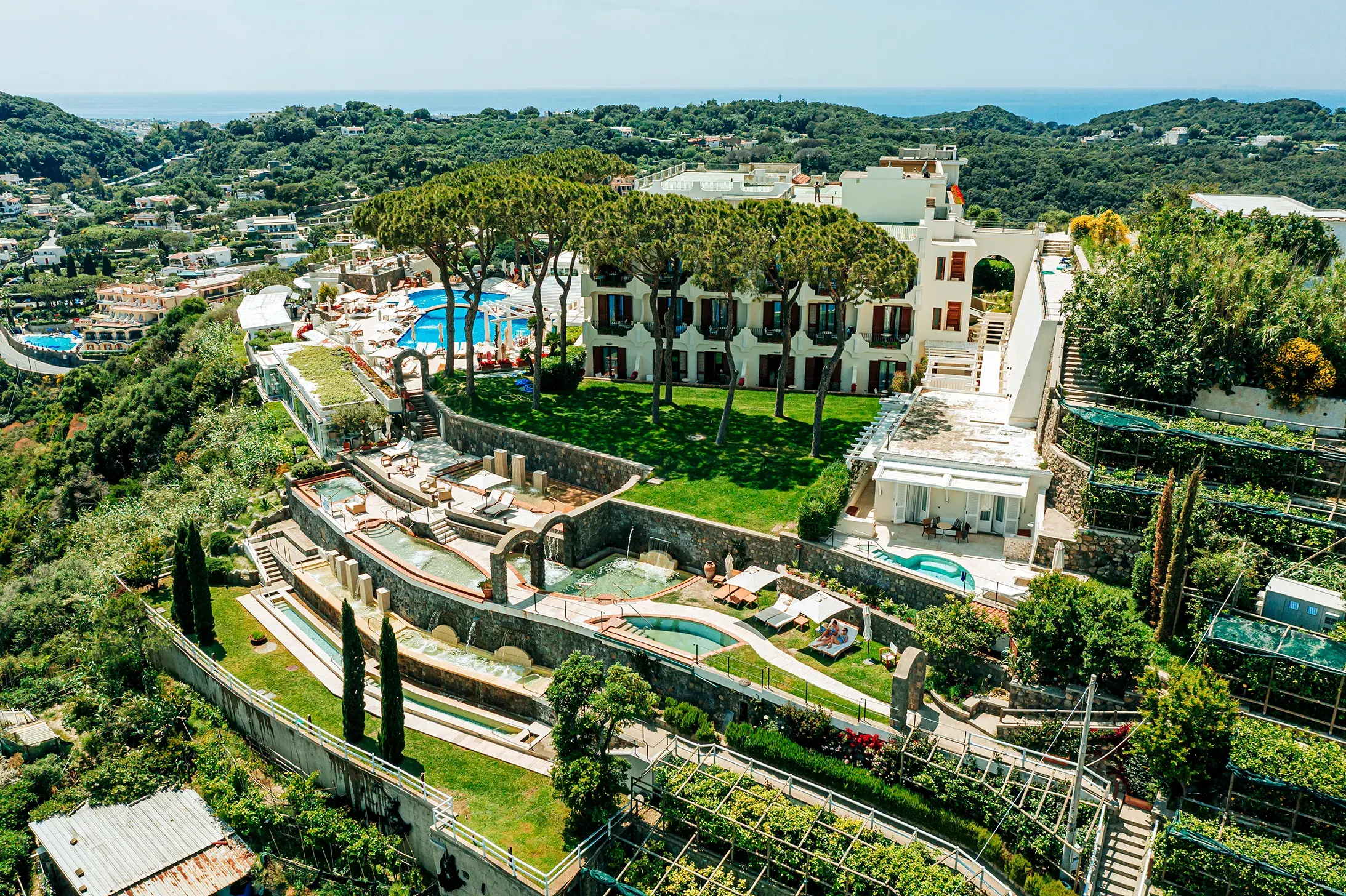 Aerial view of San Montano Resort on Ischia, featuring terraced gardens, multiple swimming pools, and lush greenery with the sea in the background.