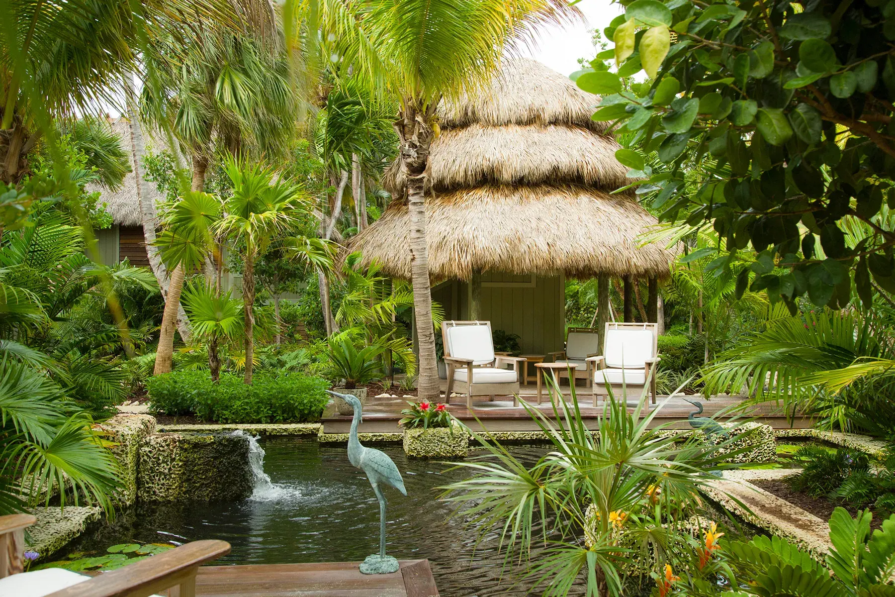 Tropical garden with thatched-roof cabana, lush palm trees, and serene pond at Little Palm Island Resort in Florida.