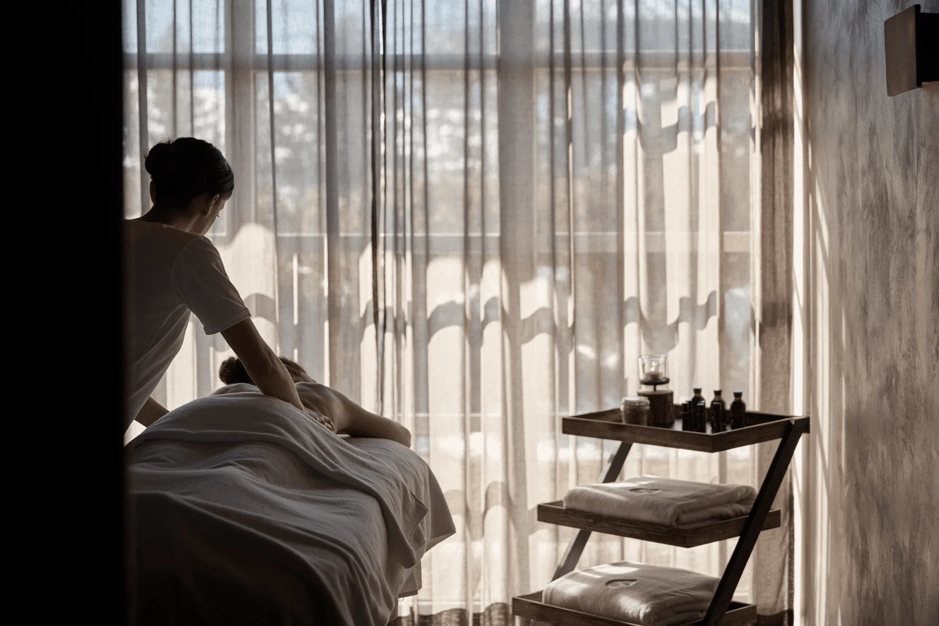 Spa treatment at COMO Alpina Dolomites with a therapist performing a relaxing massage beside softly filtered natural light.