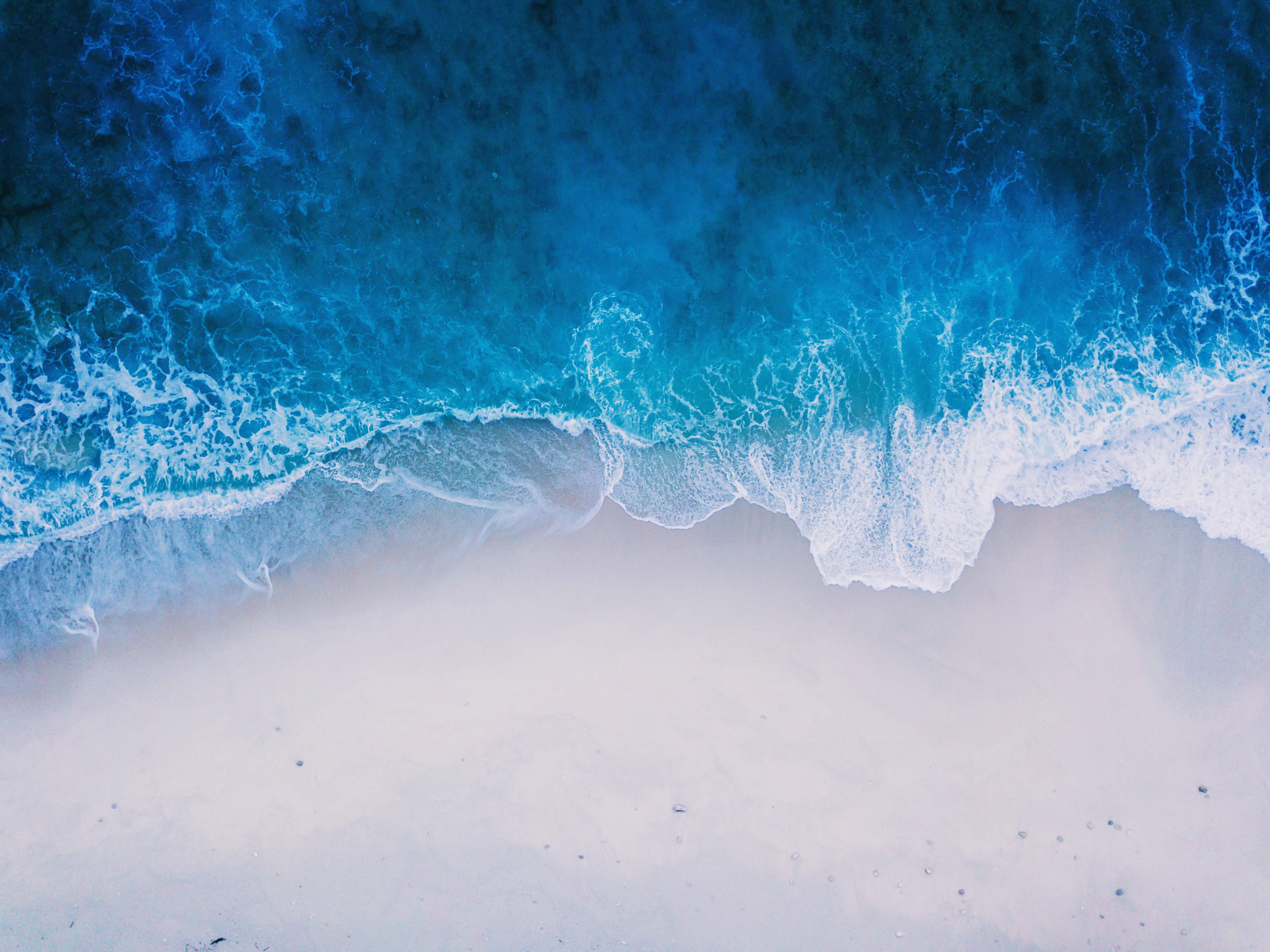 Bird's eye view of a blue ocean wavings rolling onto the sand