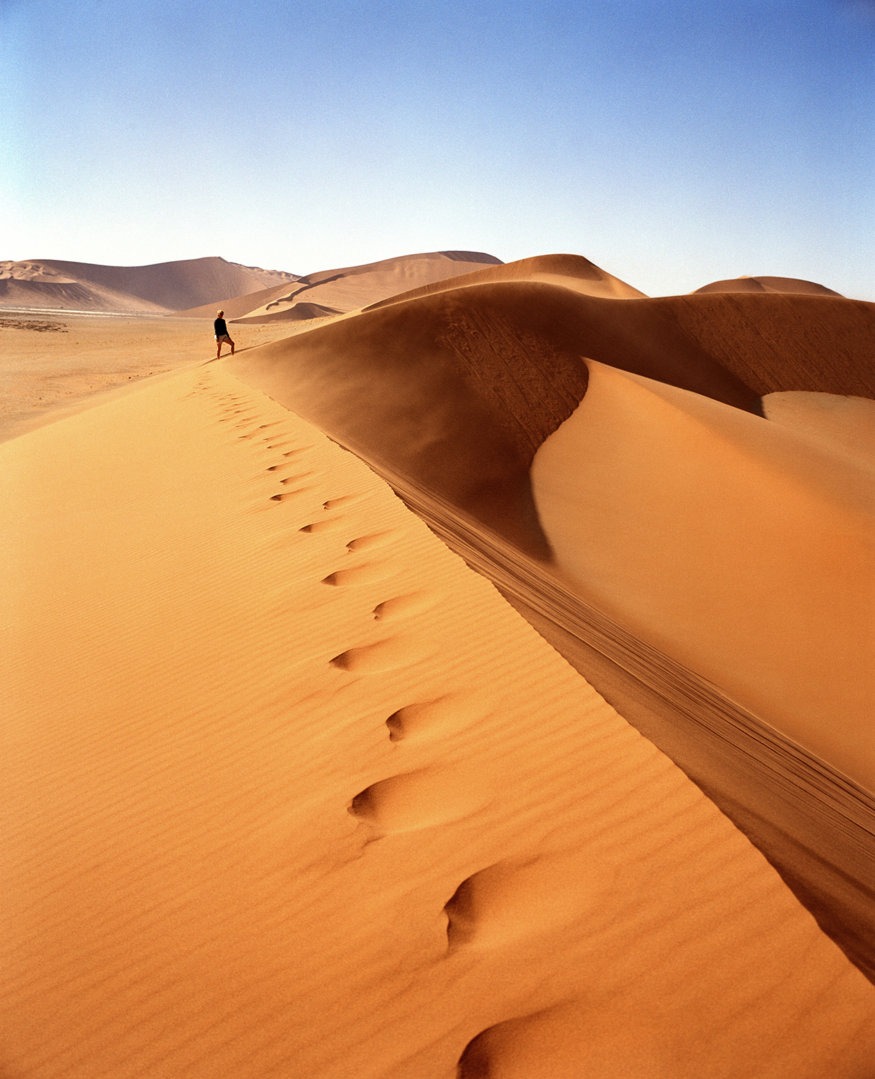Footsteps in orange desert dunes with person in the background