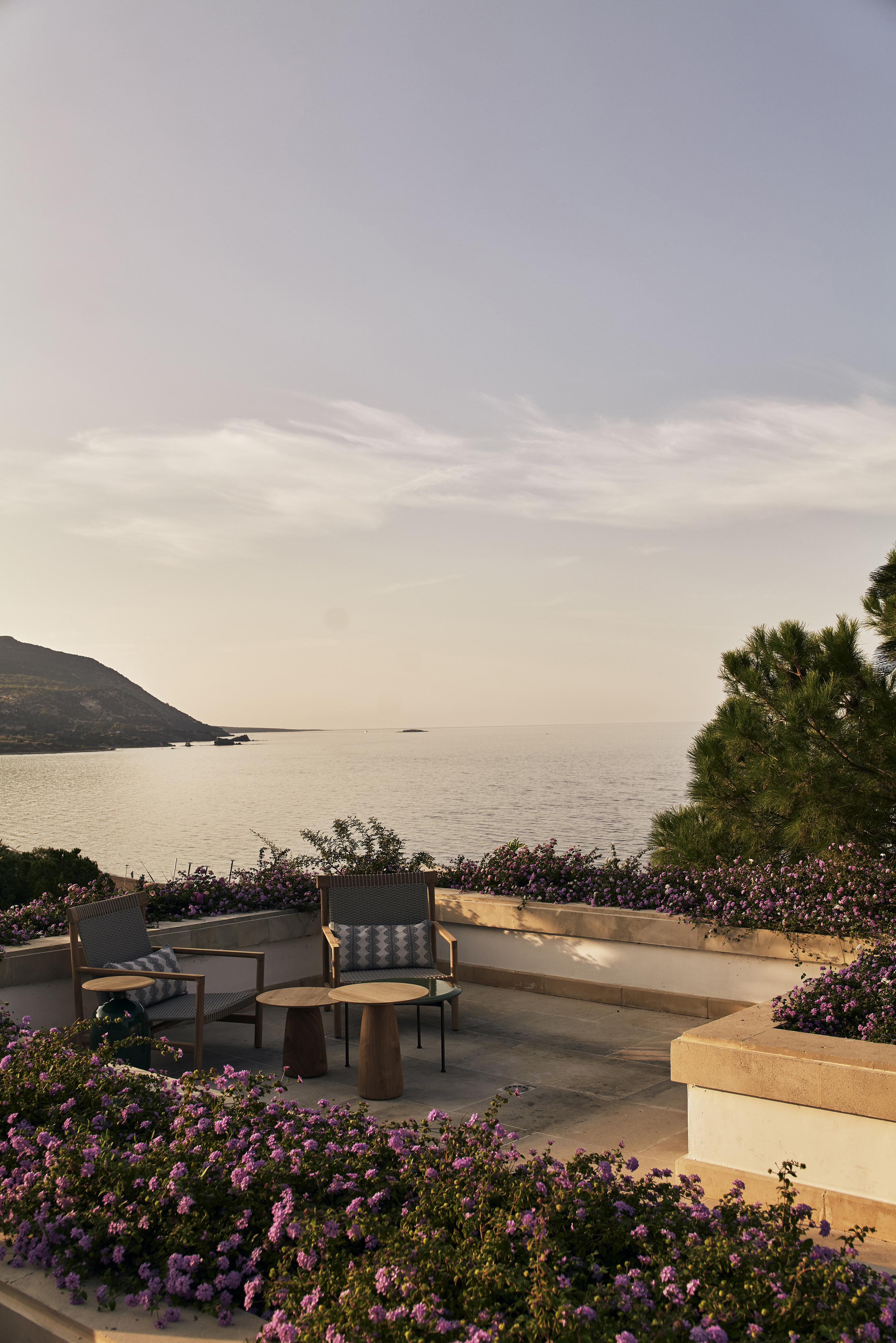 The terrace of Armonia bar at Anassa in Cyprus featuring a small table and two chairs surrounded by purple blooming bushes overlooking a sweeping view of the ocean
