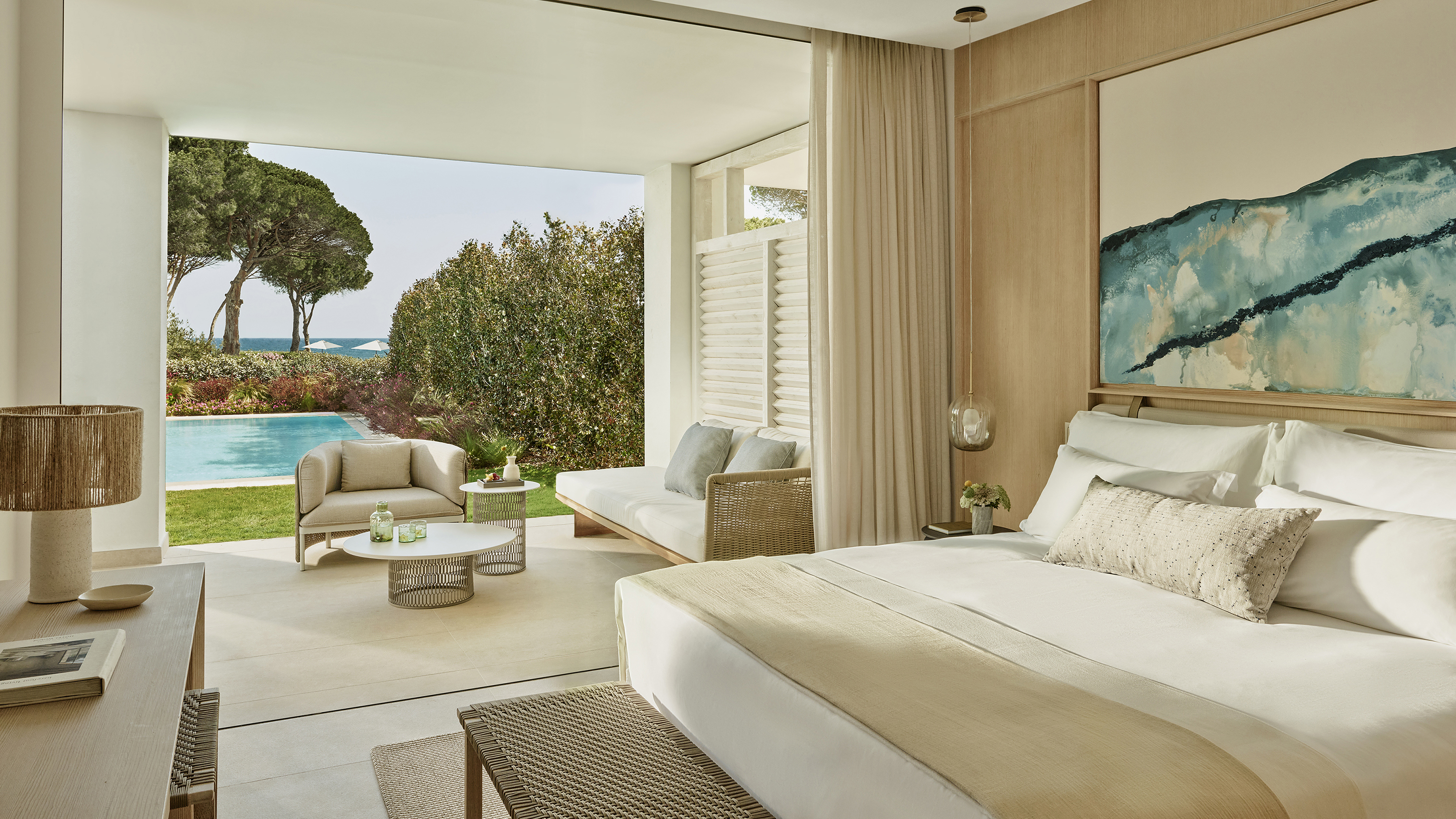A luxurious bedroom in a suite at Ikos Andalucia with furniture in neutral tones and a view of the private pool and ocean outside
