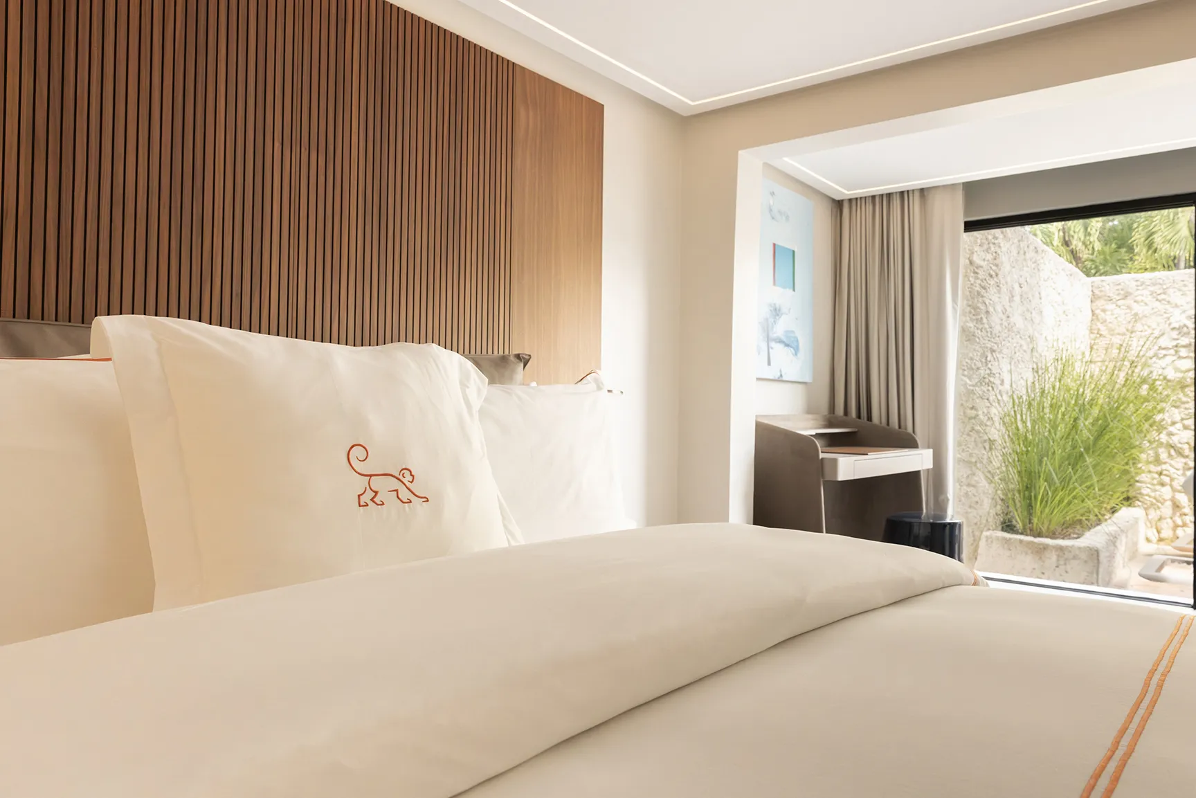Modern guest room with a neatly made bed, wood-paneled headboard, and floor-to-ceiling window overlooking a private garden.
