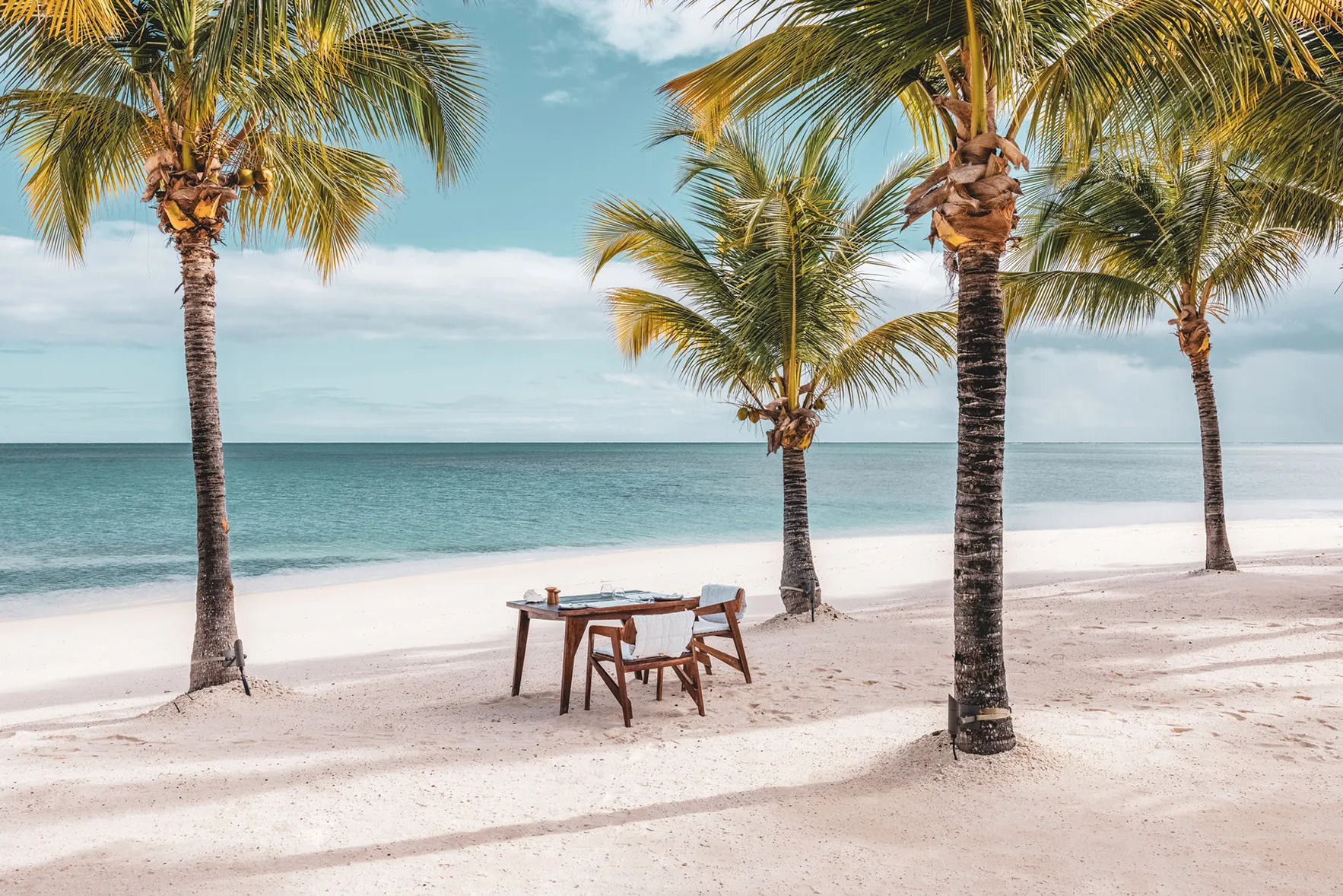 A dining table and two chairs set up for breakfast on the beach between palm trees at Miavana, Madagascar