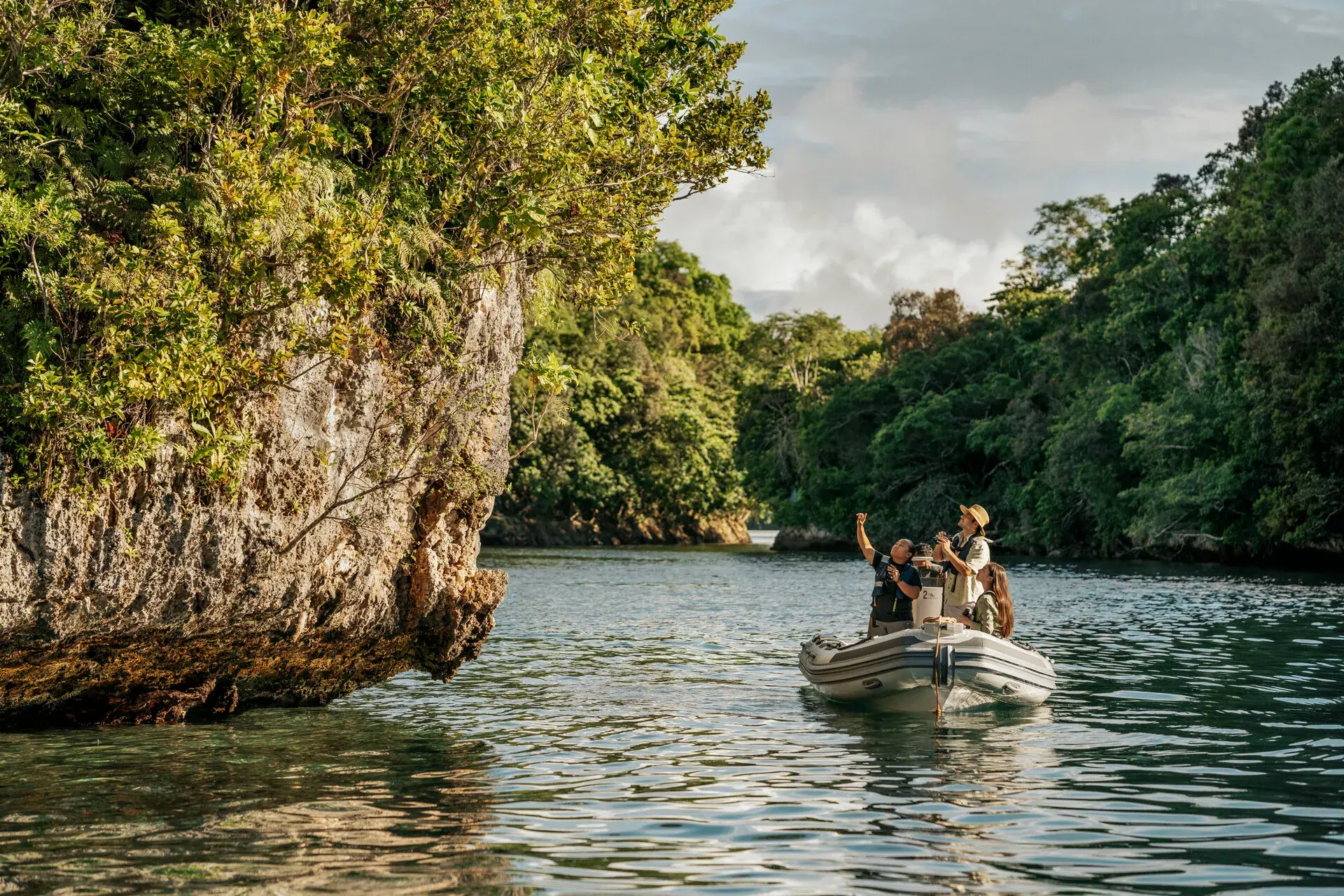 A group of guests from Four Seasons Explorer Palau in a small rib boat beside a rock formation with jungle and ocean behind