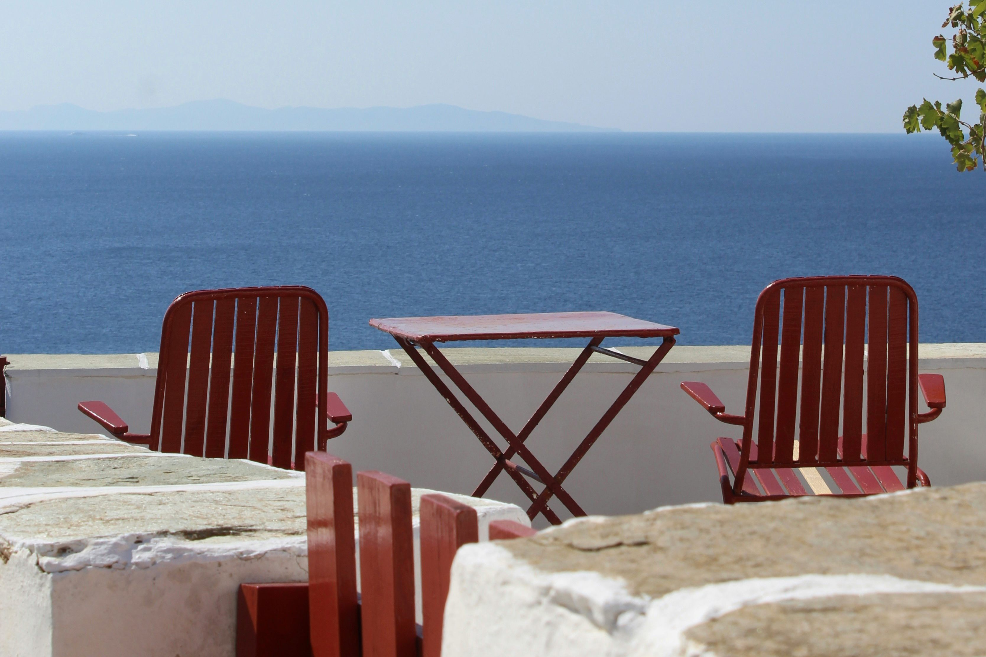 Red bistro set on a white stone terrace overlooking the Aegean sea