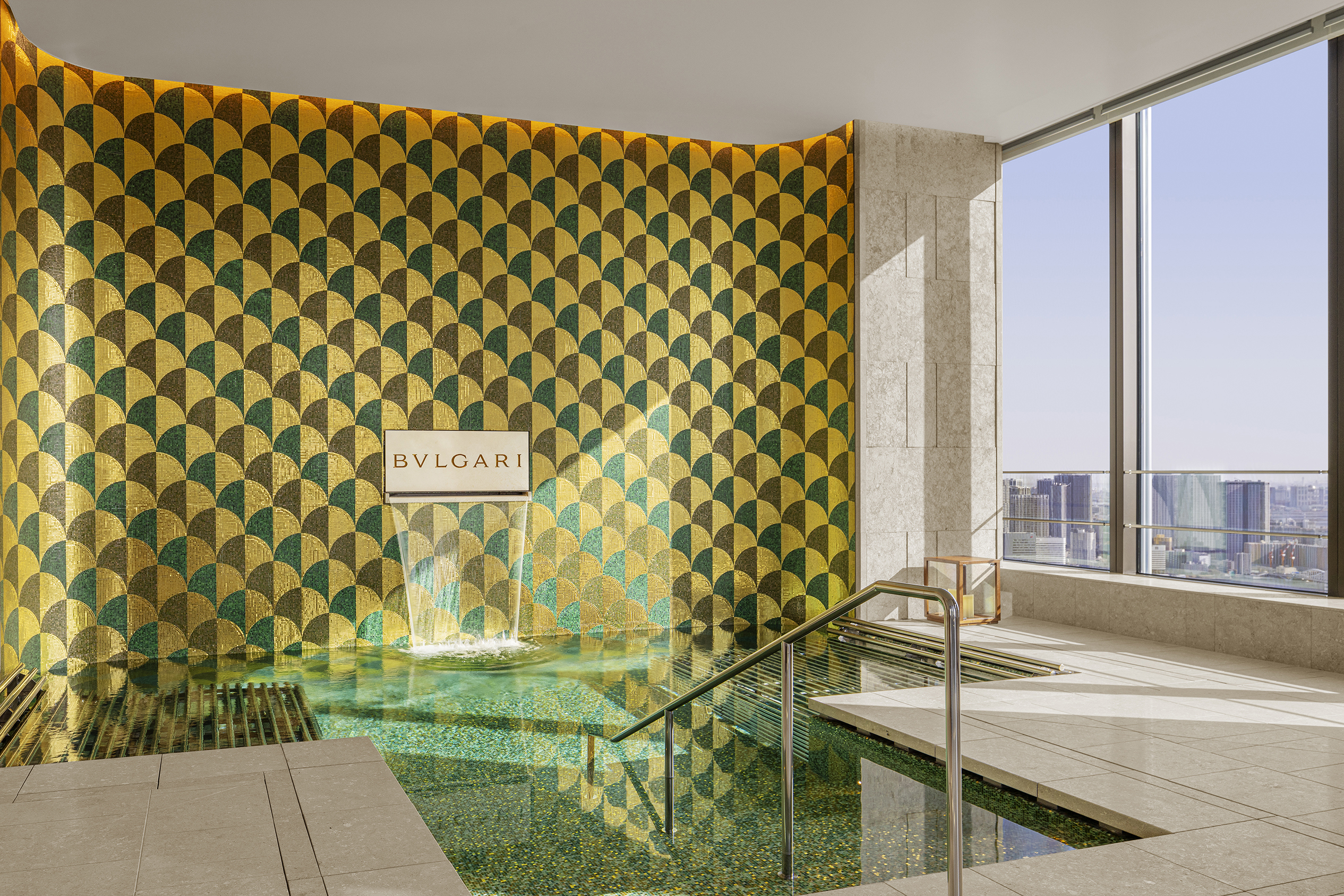 A plunge pool with a sweeping city view and a decorative wall with the Bvlgari logo