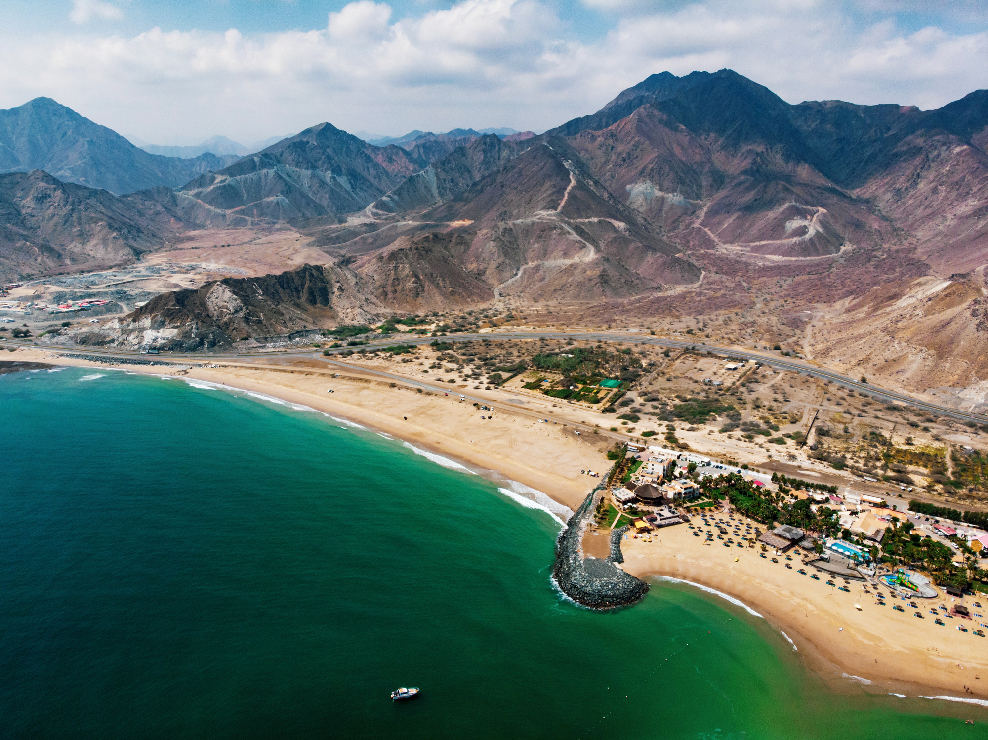 Aerial view of a coastal landscape with mountains, a sandy beach, and clustered buildings.