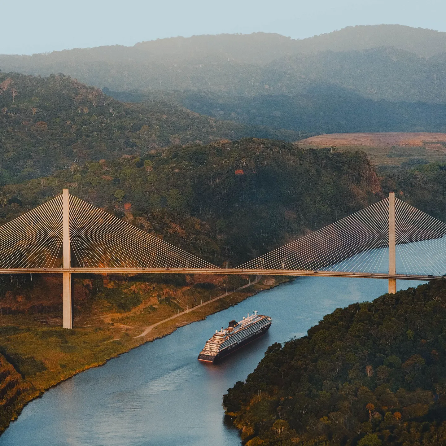 Cruise, Explora Journeys, Explora III cruise ship sailing under a bridge between forest-covered hills