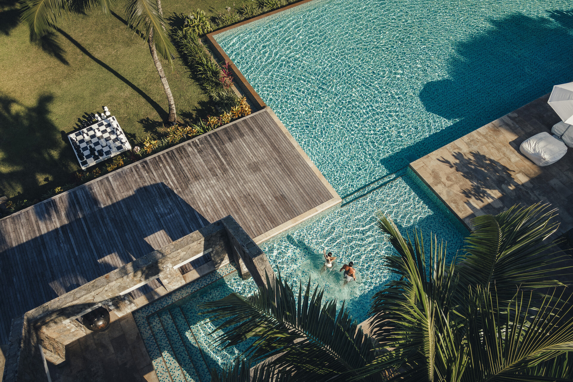 Couple in villa pool with large chess set on lawn