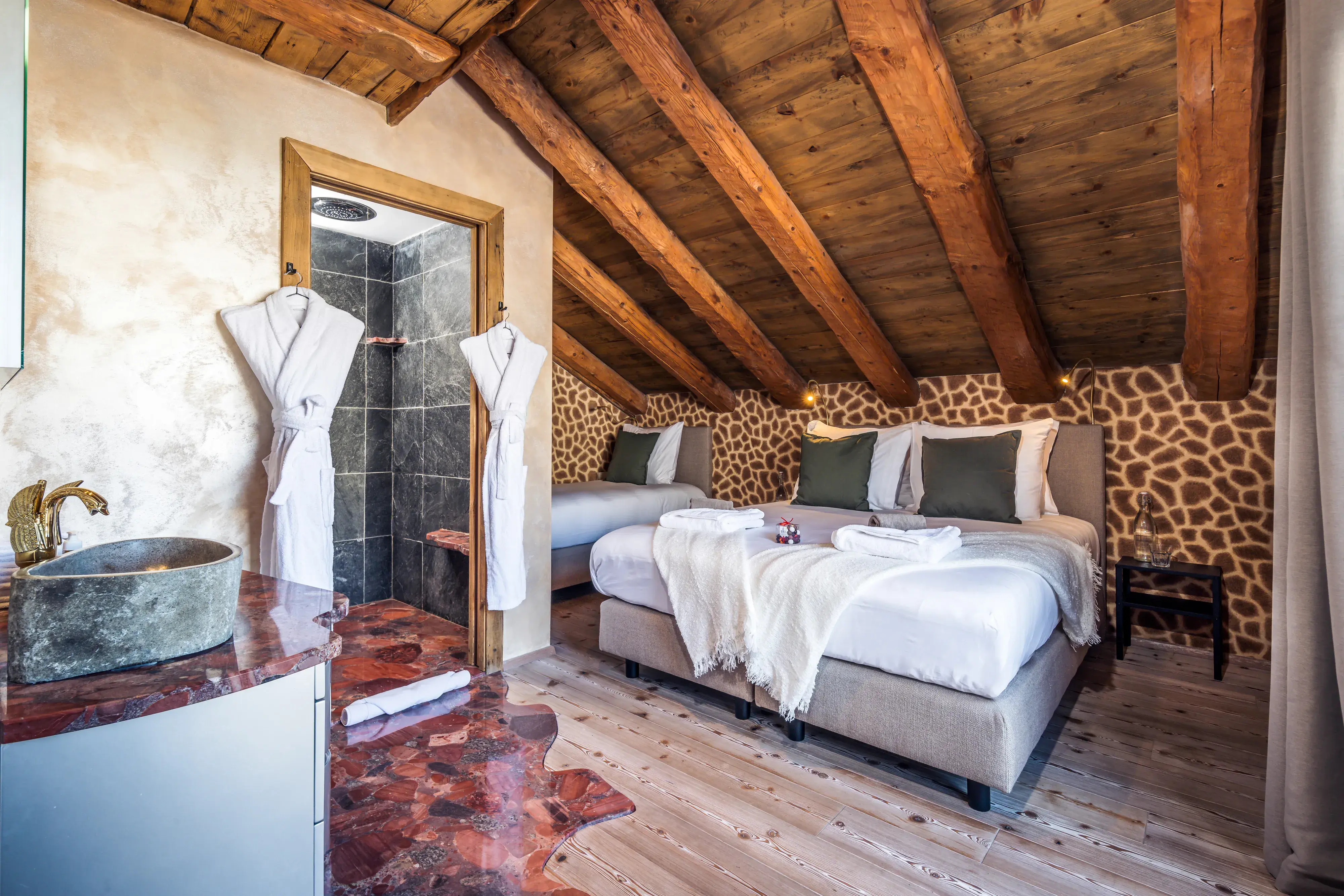 Guest room in Chalet Cheval Blanc featuring traditional wooden ceilings, three beds, robes. quirky giraffe wallpaper and an ensuite bathroom with tiles leading from the door to a sink with an ornate tap
