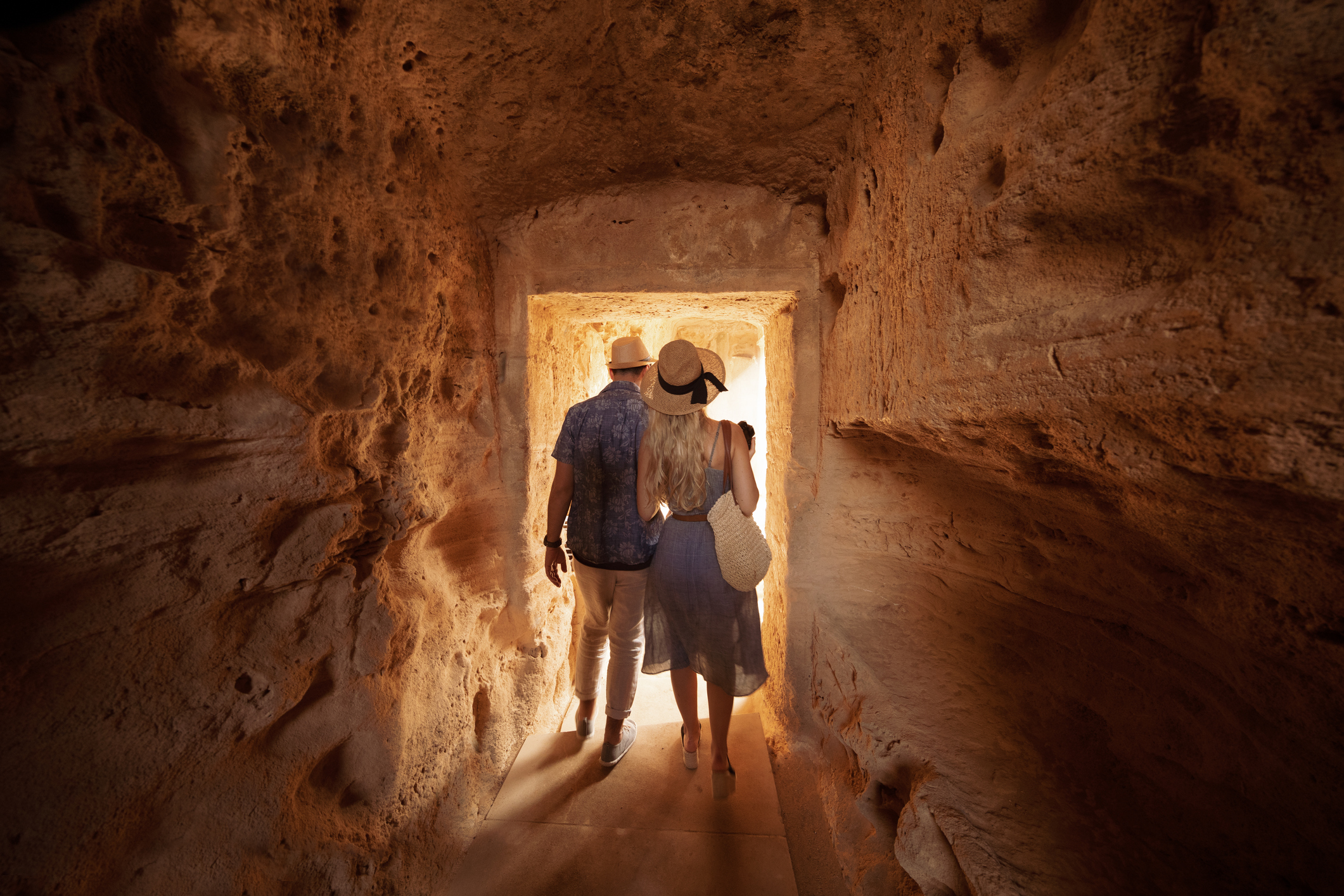 A couple is seen from the back as they walk through a tunnel in an ancient stone structure