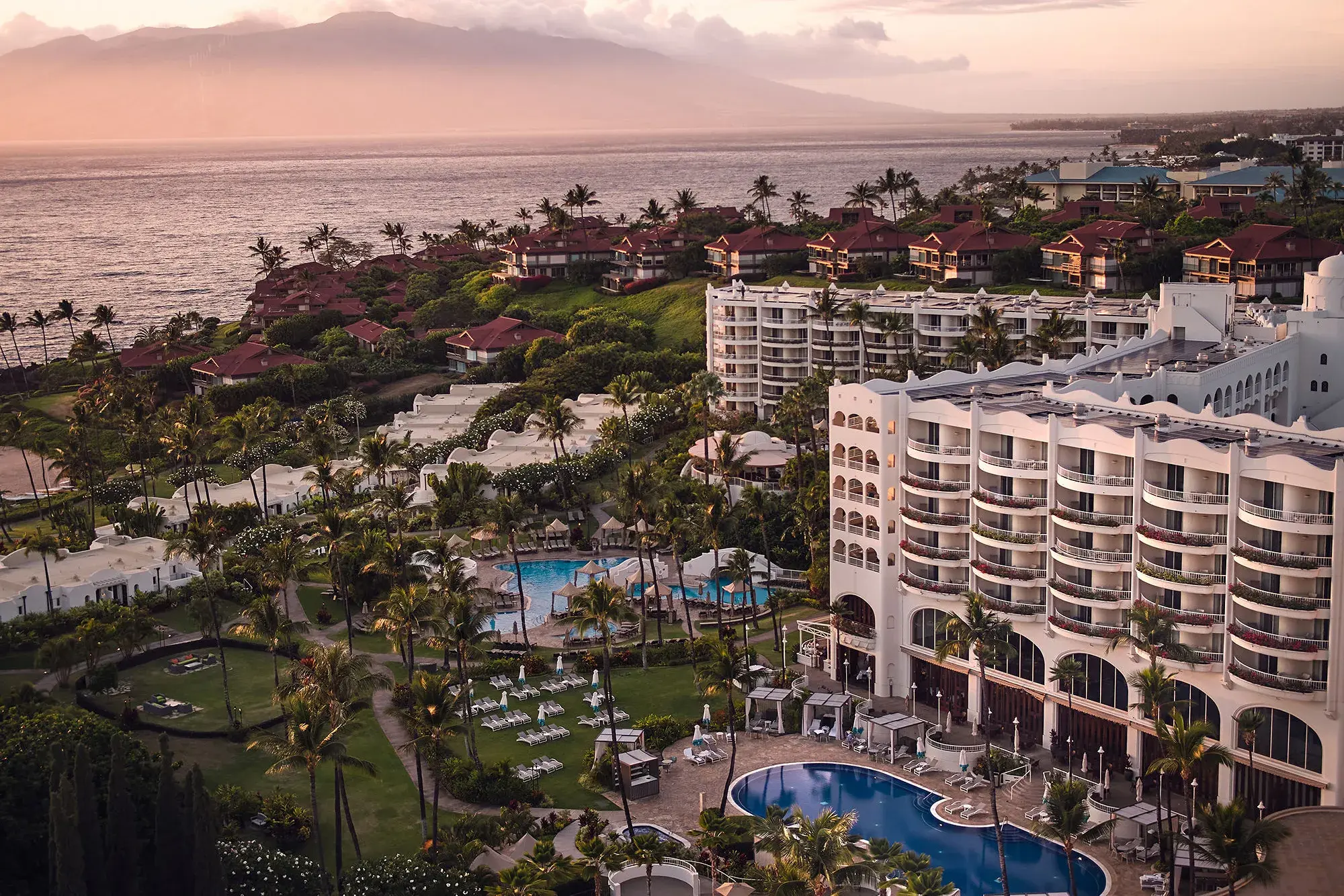 Aerial view of Fairmont Kea Lani featuring a white multi-storey building, swimming pools, lush gardens and red roofed villas with the ocean in the background