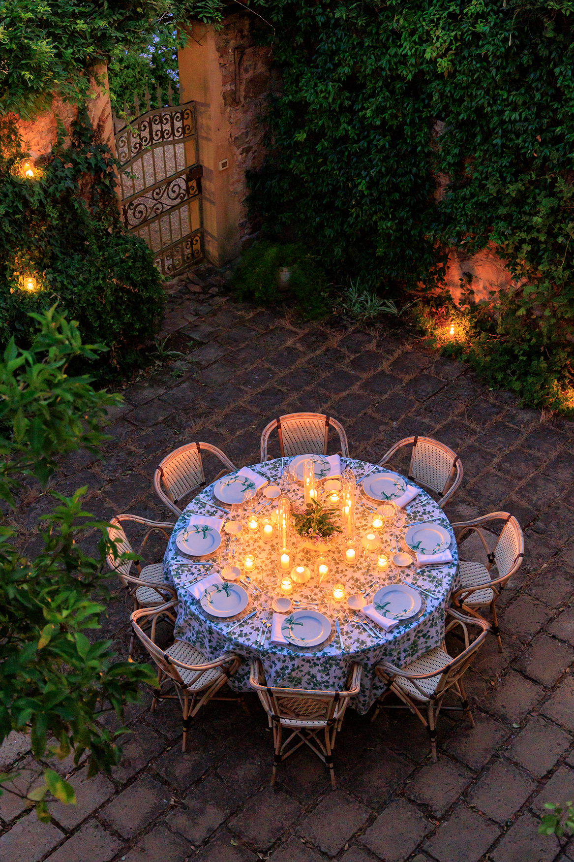 A circular table with eight chairs set for dinner by candlelight in a private garden 
