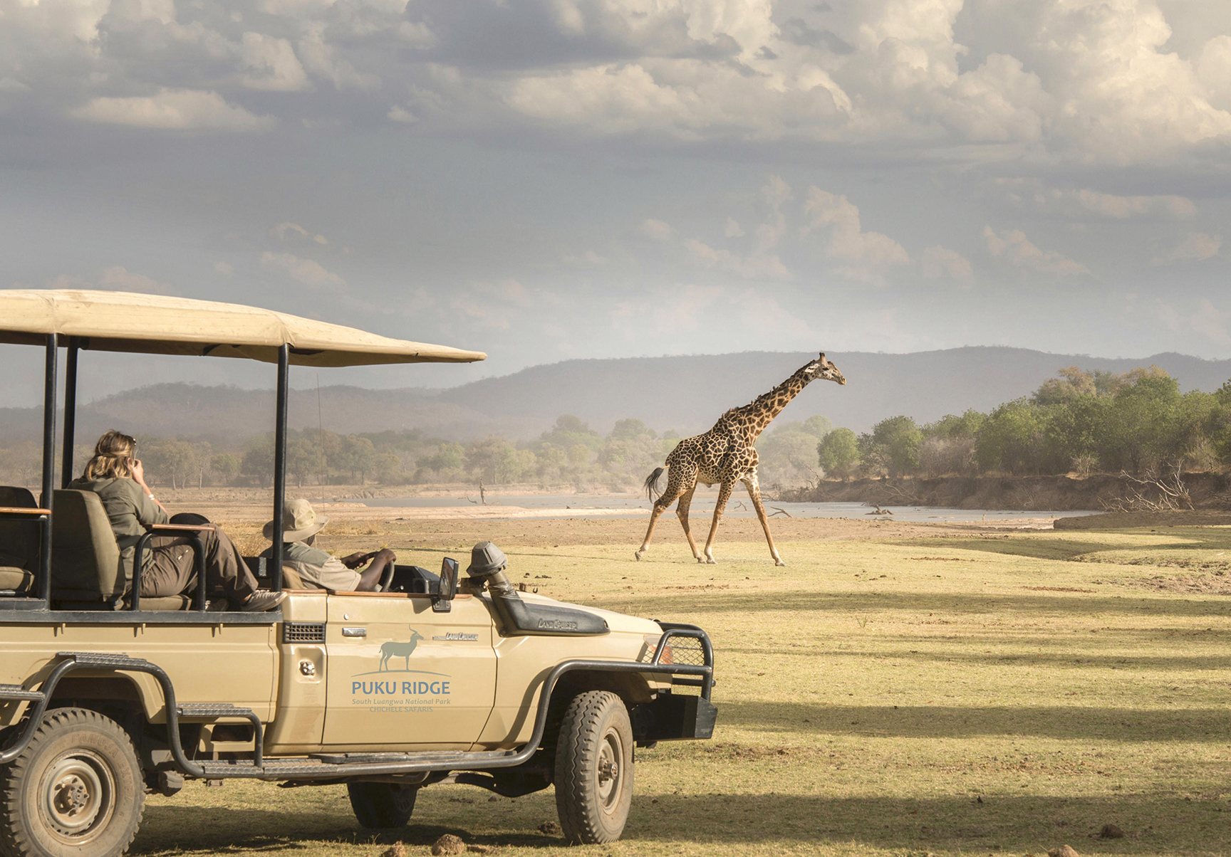 Africa, Zambia, South Luangwa National Park, Puku Ridge Camp, people in game drive jeep photographing a giraffe
