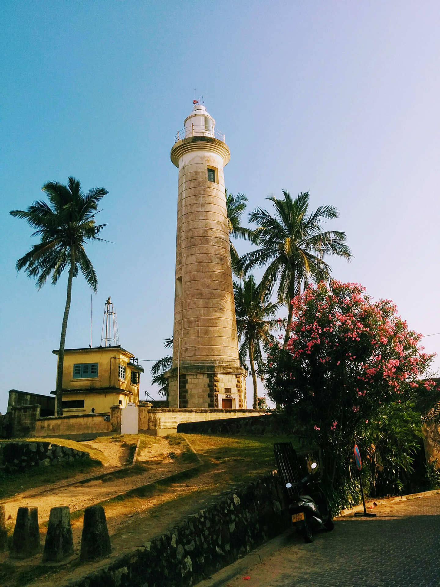 White and brown lighthouse near green trees under a blue sky