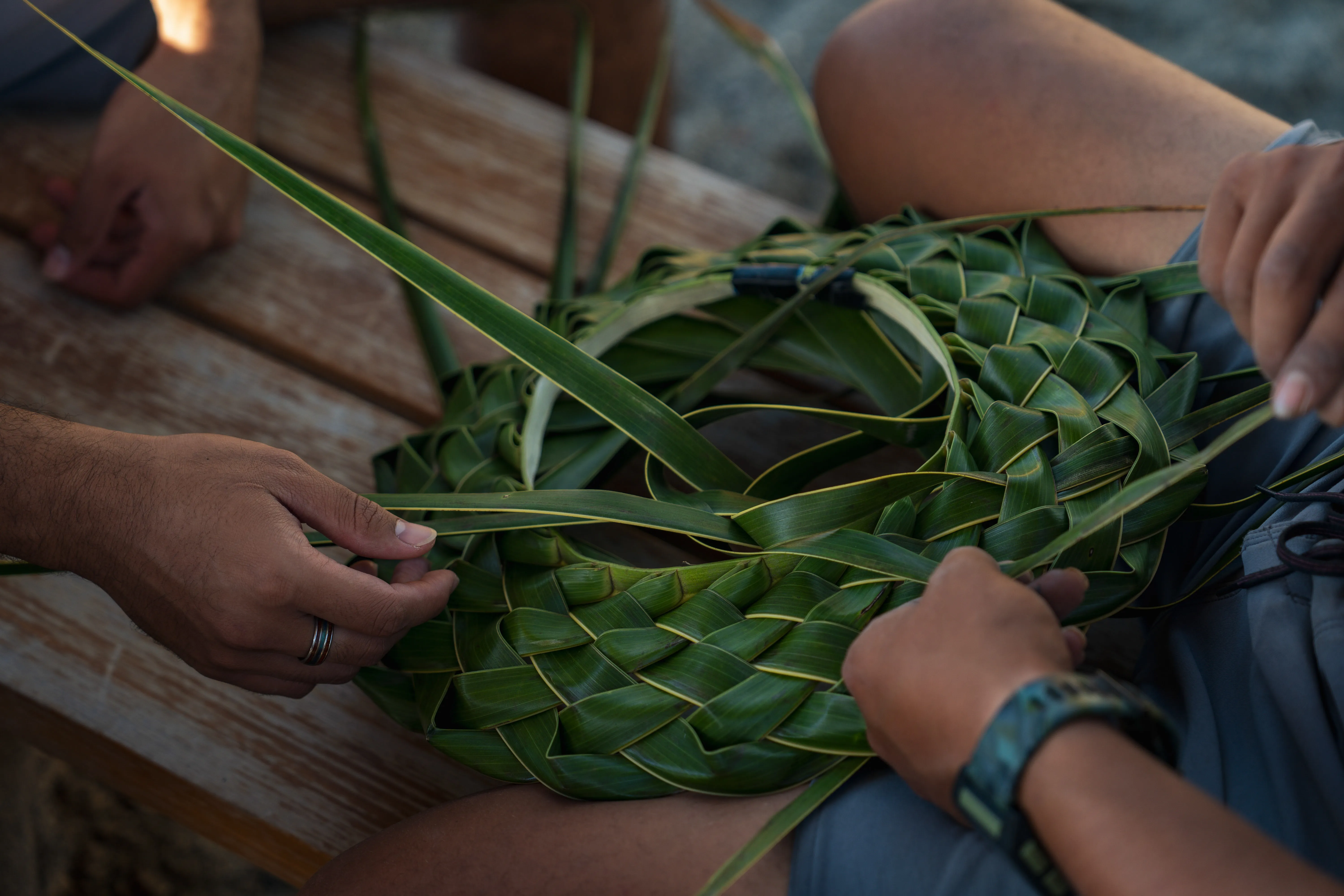 Two people weaving a traditional basket from leaves
