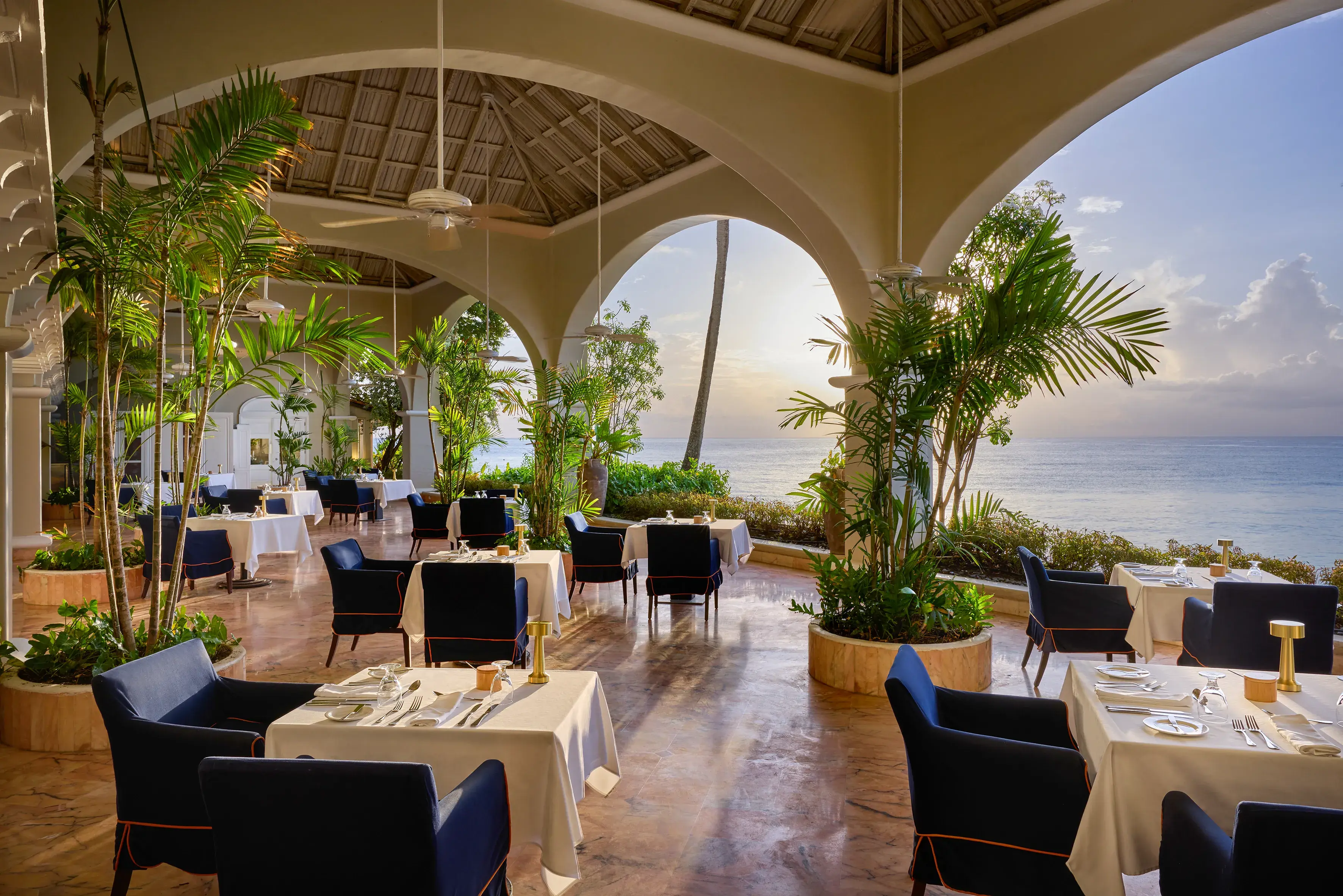Palm Terrace at Fairmont Royal Pavilion in Barbados featuring elegant dining tables and palm plants with sweeping ocean views