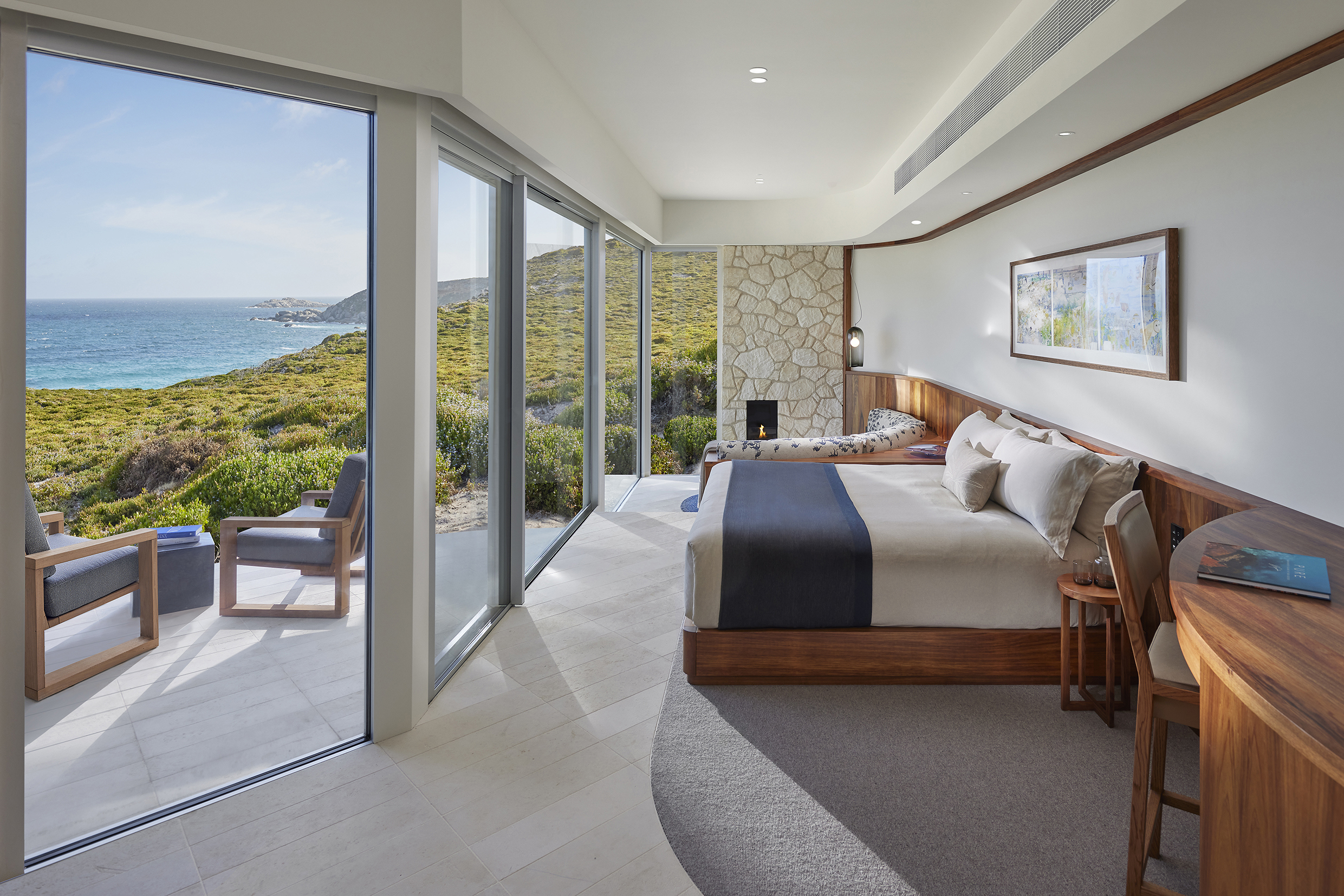 A large suite at Southern Ocean Lodge with wooden furniture and long wall of floor-to-ceiling windows looking out to the ocean