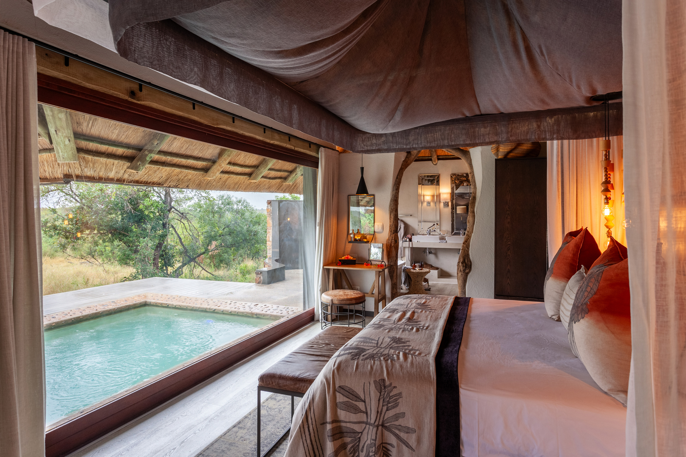 Plush bed with accent pillows facing an outdoor deck with pool