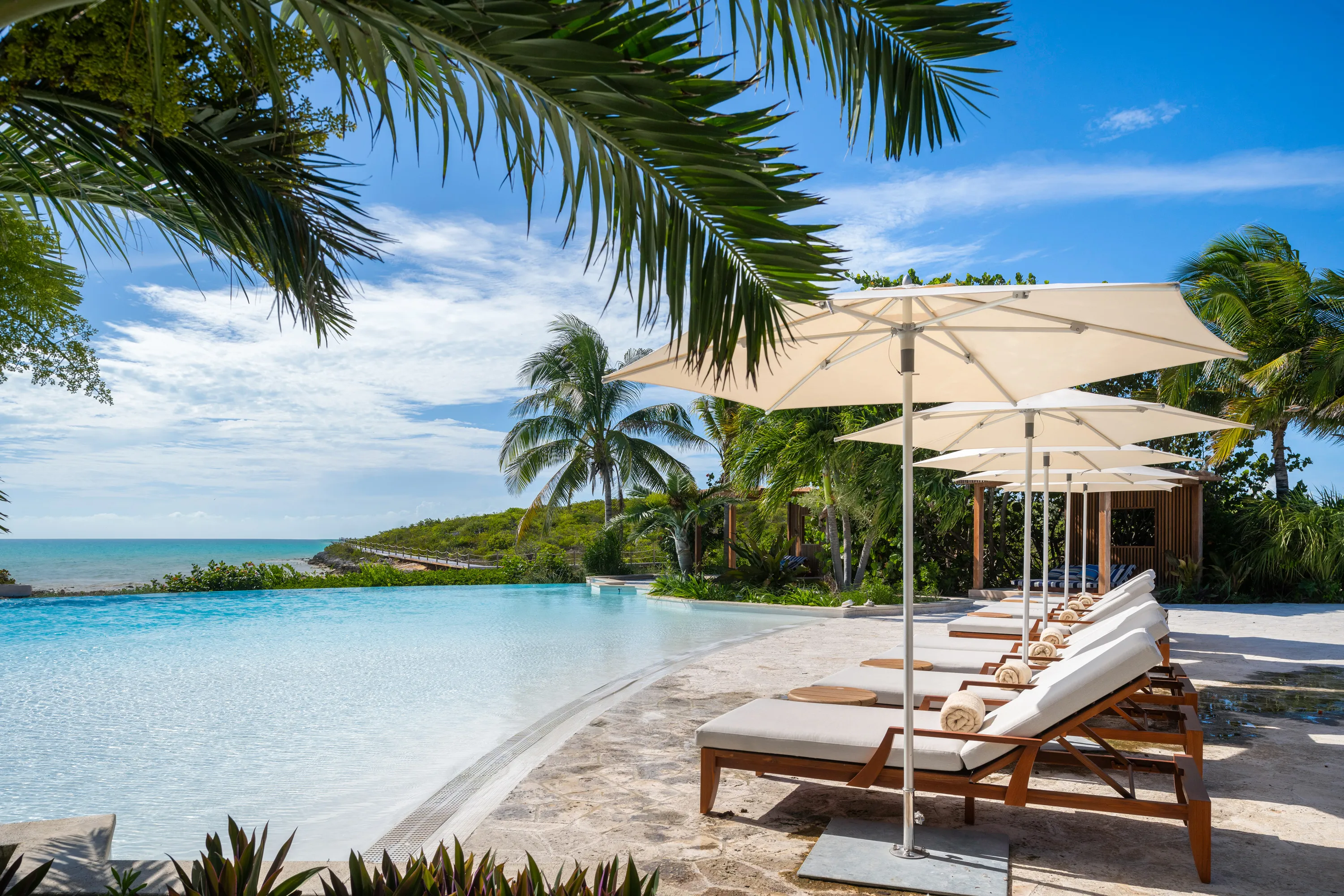 Pool and loungers at Ambergris Cay in Turks & Caicos featuring loungers lined up beside an infinity pool surrounded by palms with the ocean beyond
