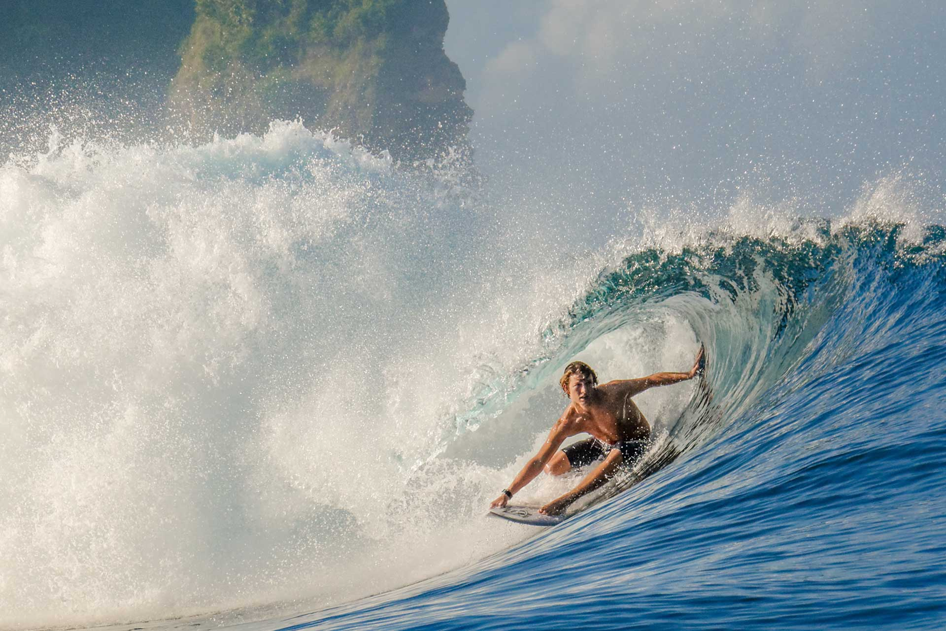 Surfer riding inside a powerful breaking wave with spray cascading overhead.