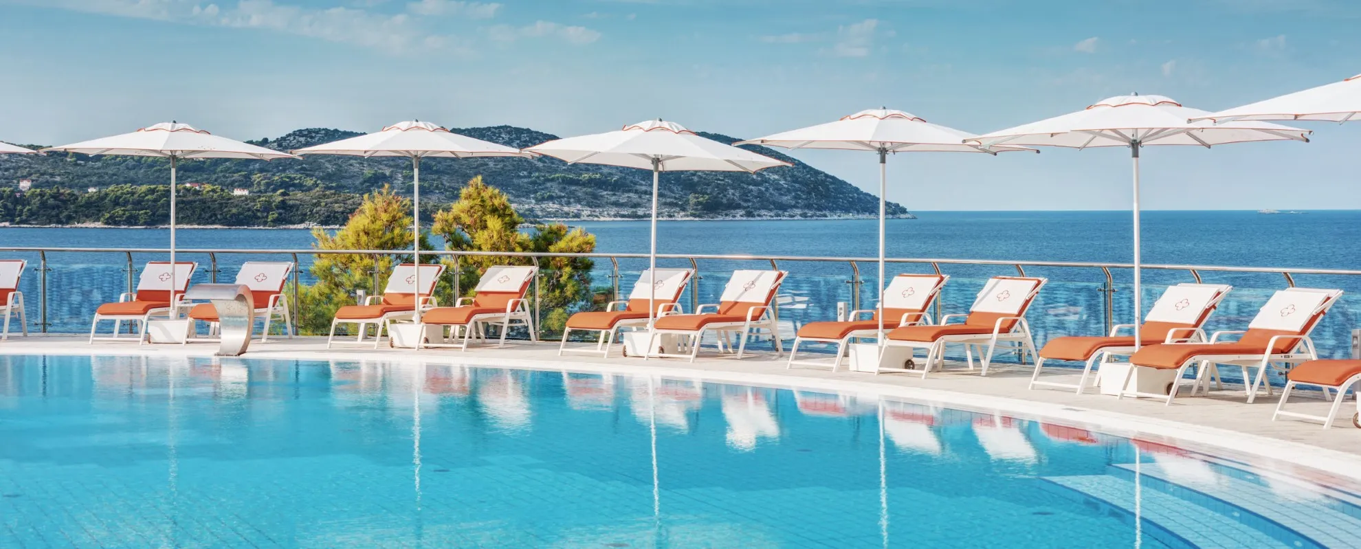 Orange and white sun loungers and parasols around the pool at Villa Dubrovnik, with a sea view in the background