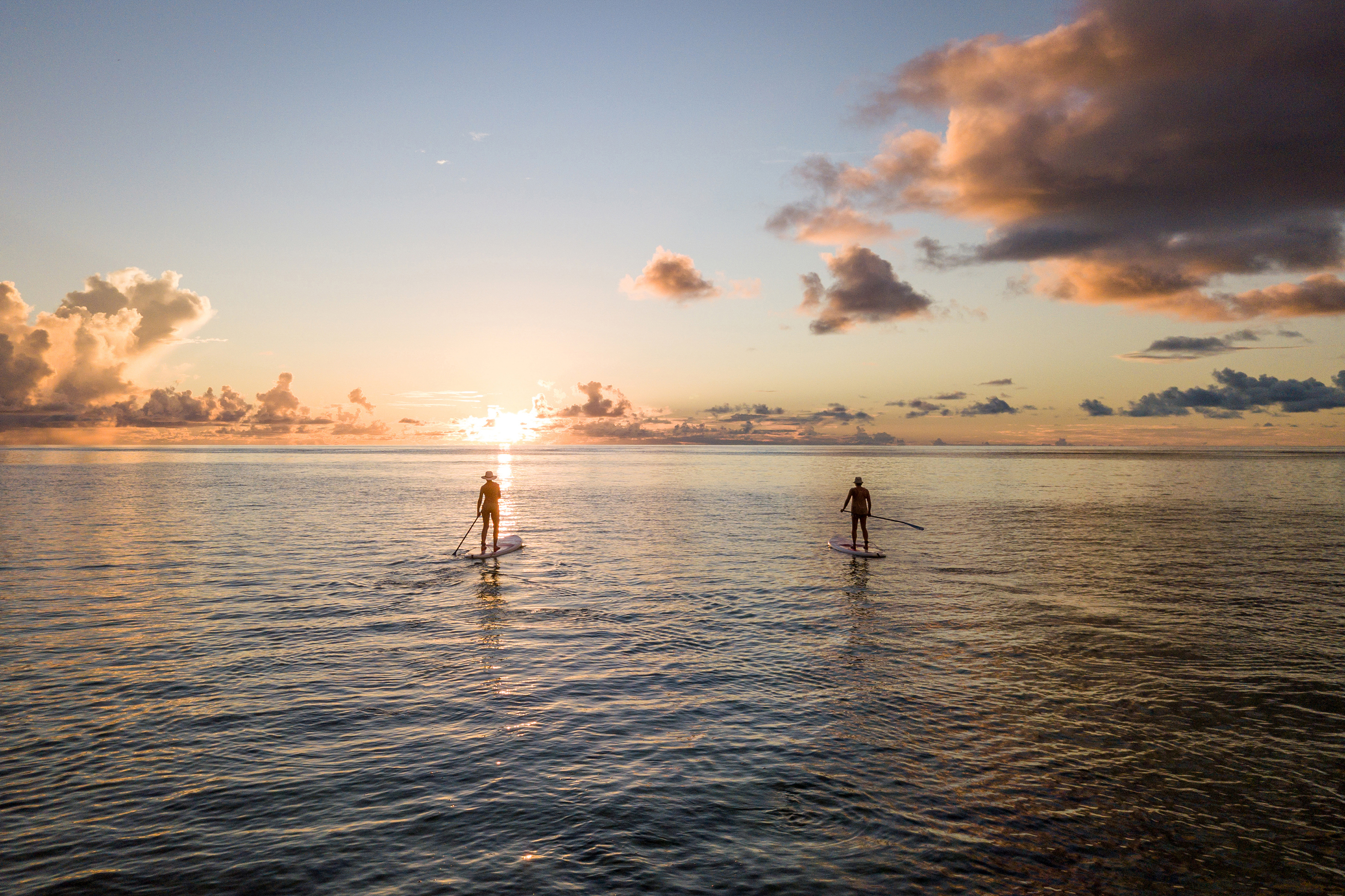 A couple paddle boarding on a calm ocean at sunset