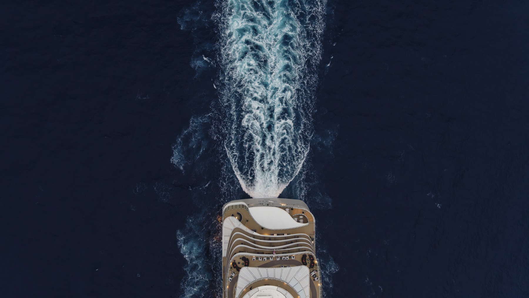 Aerial view of the stern of a Silversea cruise ship sailing through the ocean, leaving a trail of white water behind it.
