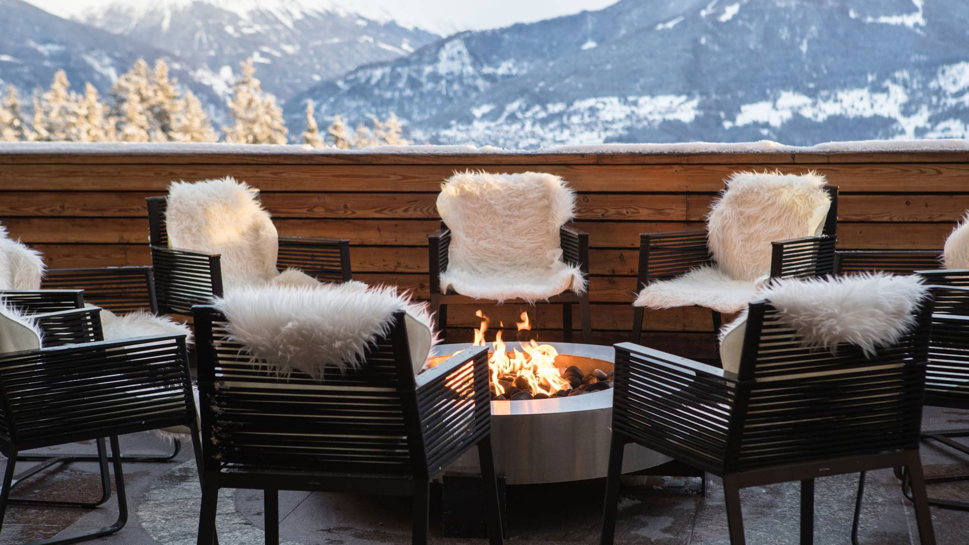 Black chairs with white fluffy covers circled around a fire